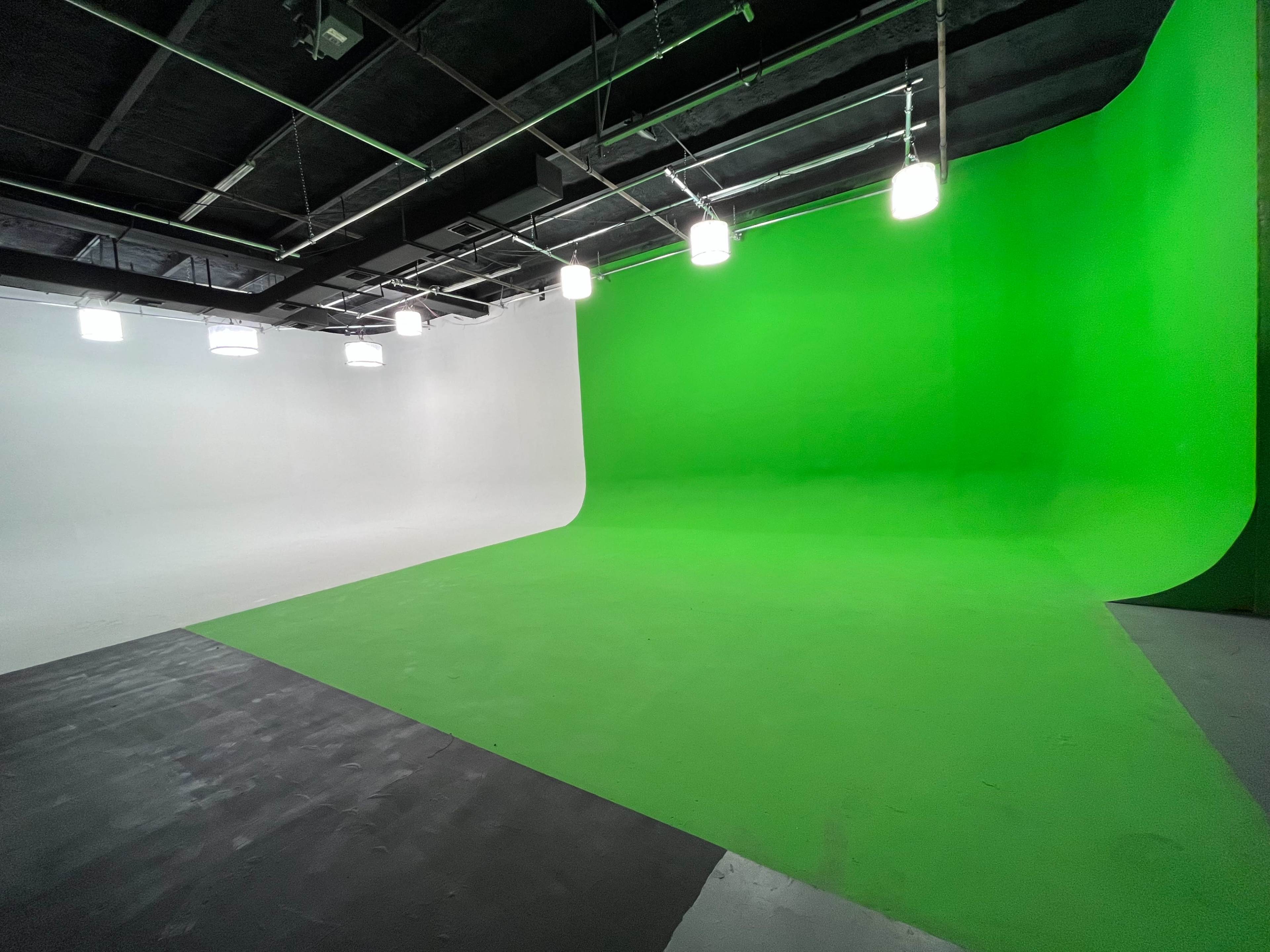 A studio with a white background on one side and a green screen backdrop on the other, illuminated by overhead lights.