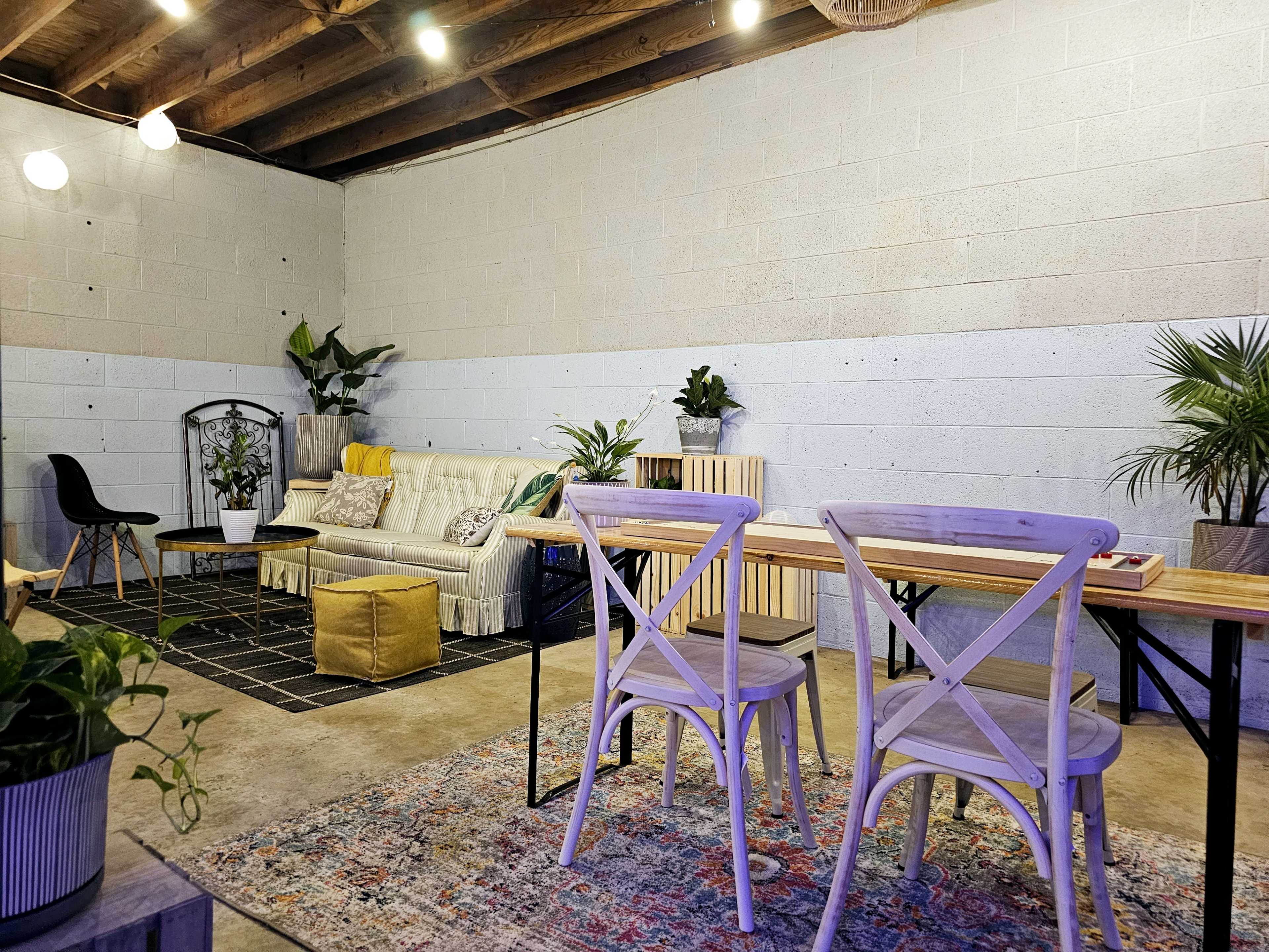 A modern interior space features a sofa, dining table with chairs, and various indoor plants against a light gray wall.