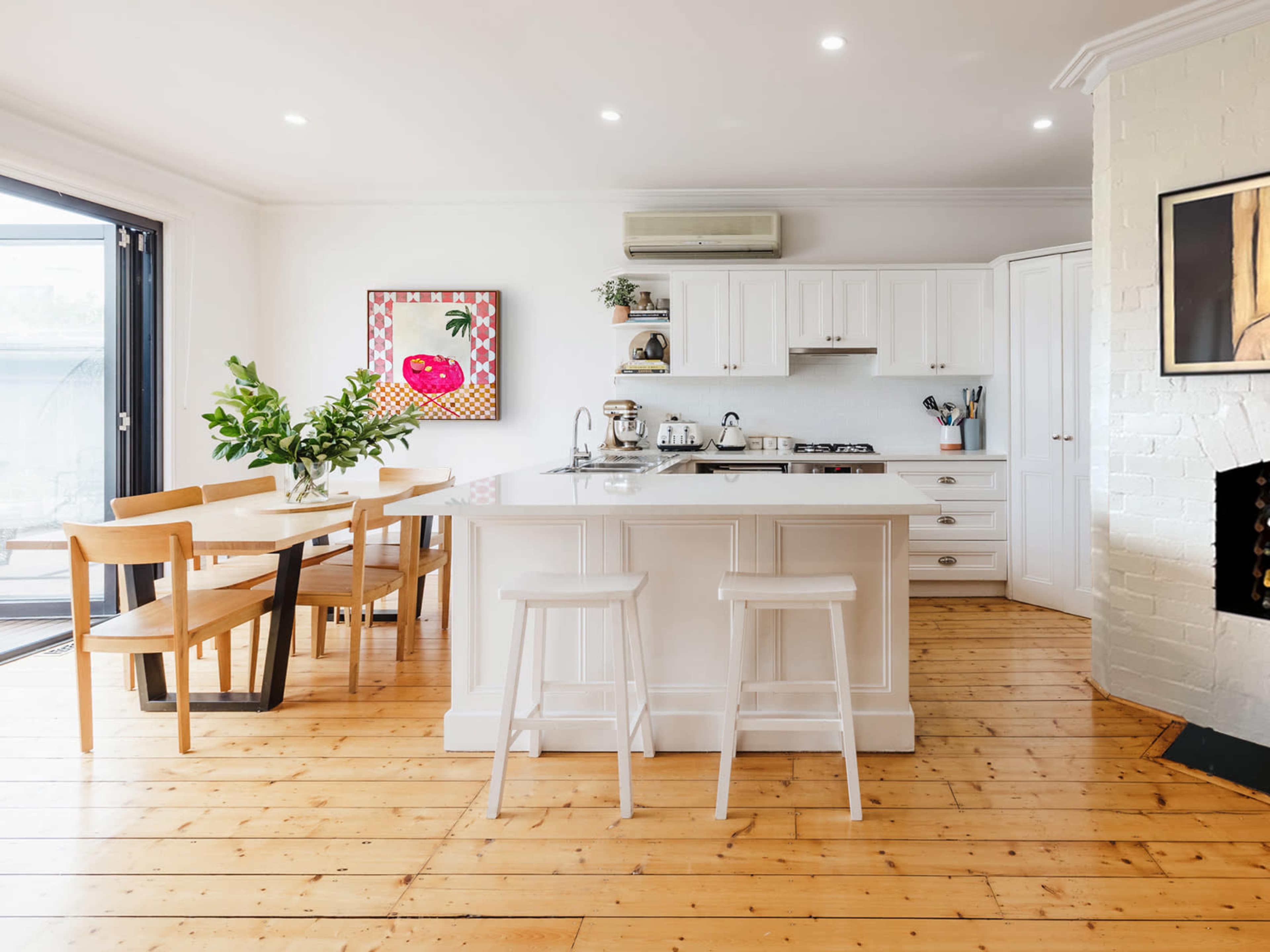 A modern kitchen features a central island, wooden flooring, and a dining area with a table and chairs.