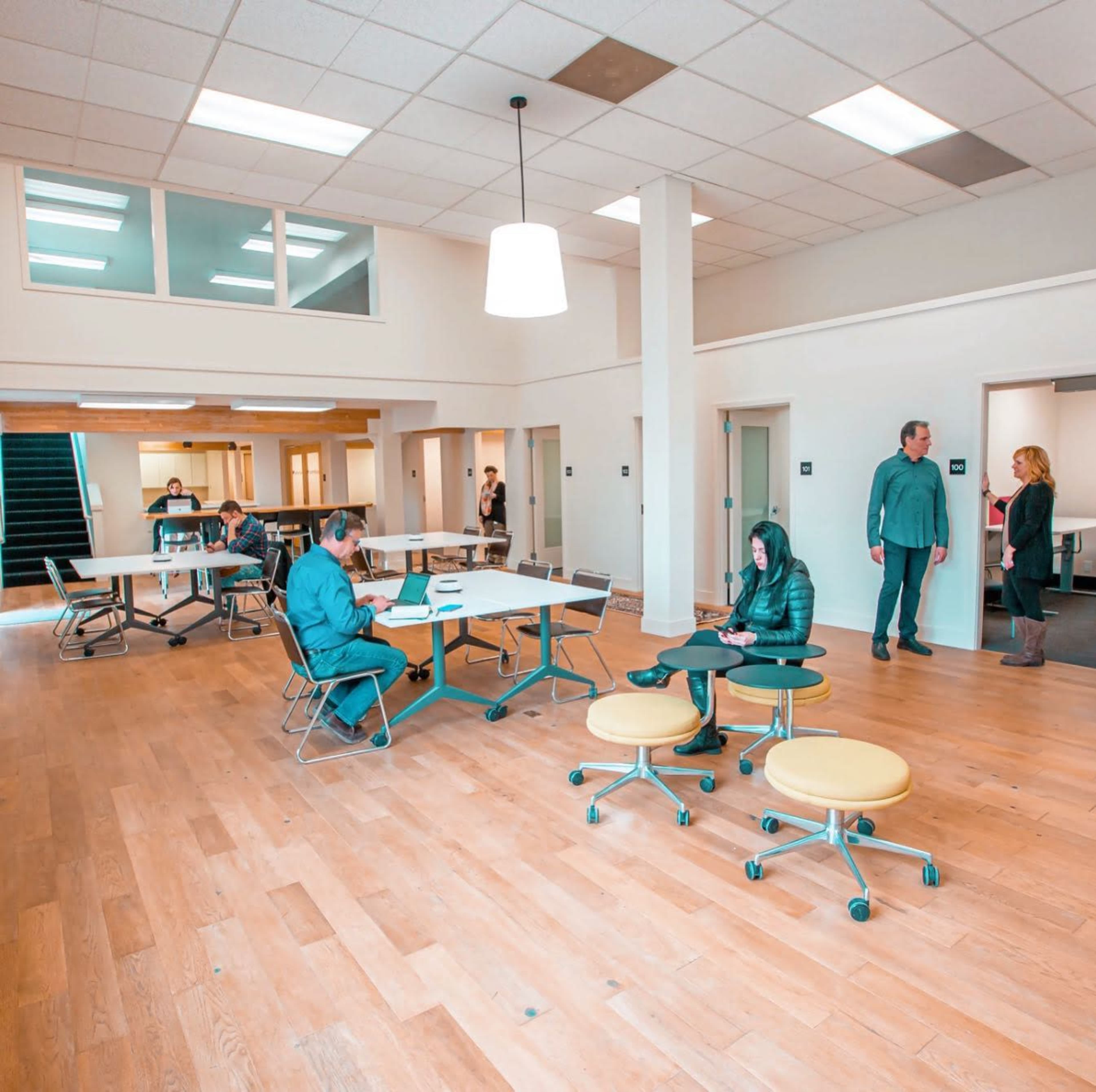 A spacious room with several tables and chairs, featuring people engaged in conversation and work at various locations.