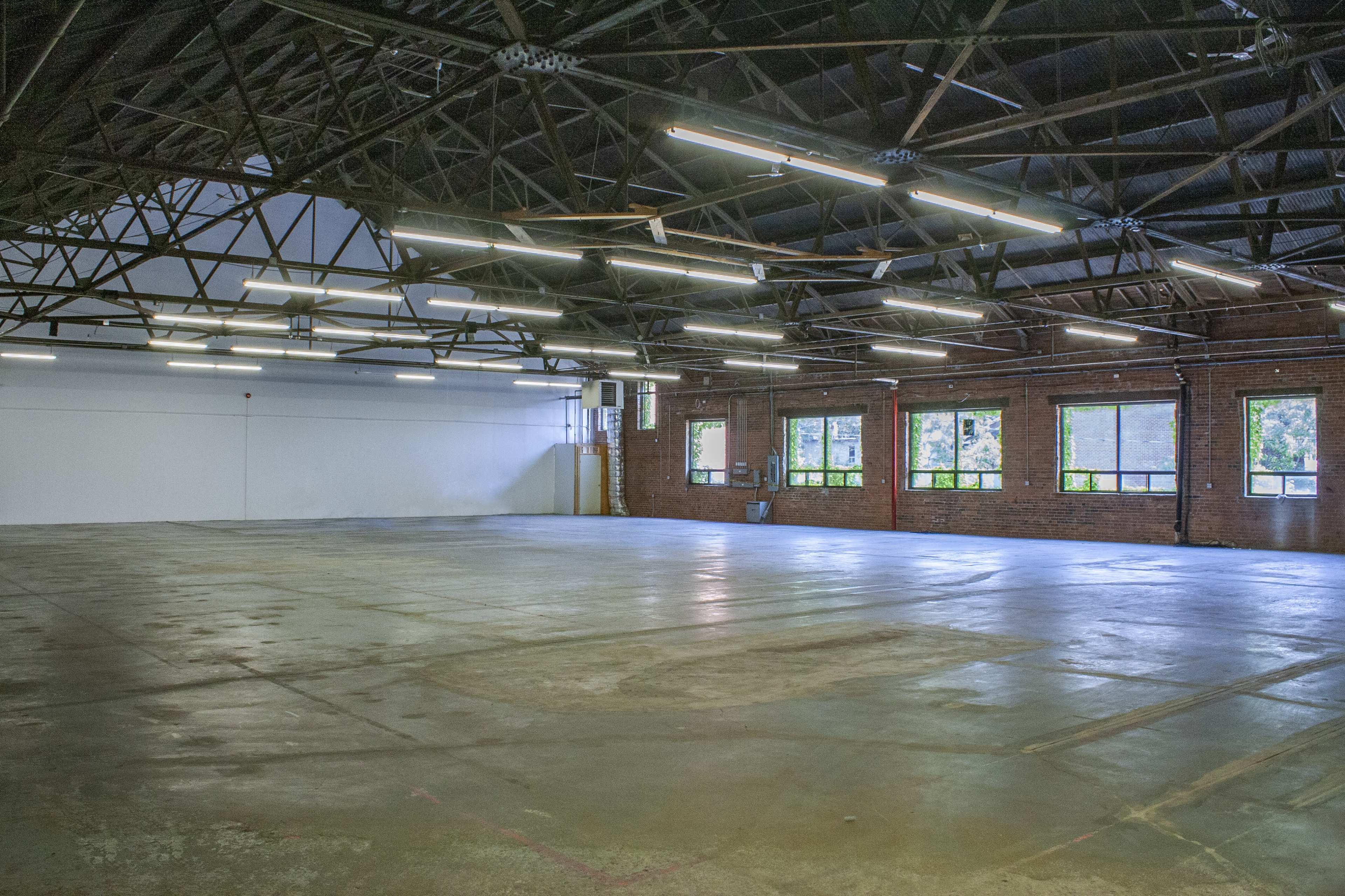 A spacious, empty industrial room with large windows and exposed beams.