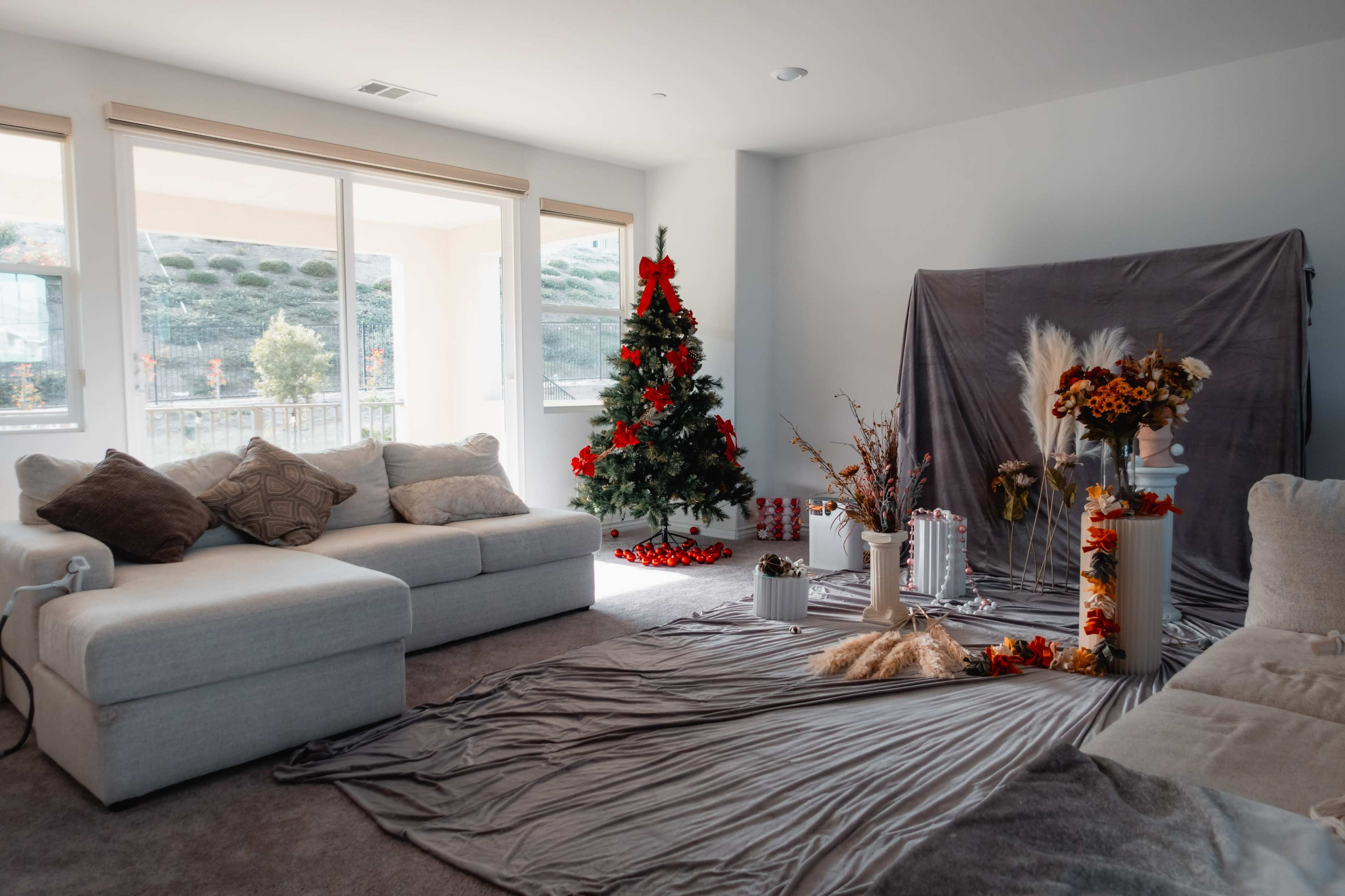 The scene depicts a cozy living room featuring a decorated Christmas tree, a gray backdrop, and seasonal decorations on the floor.