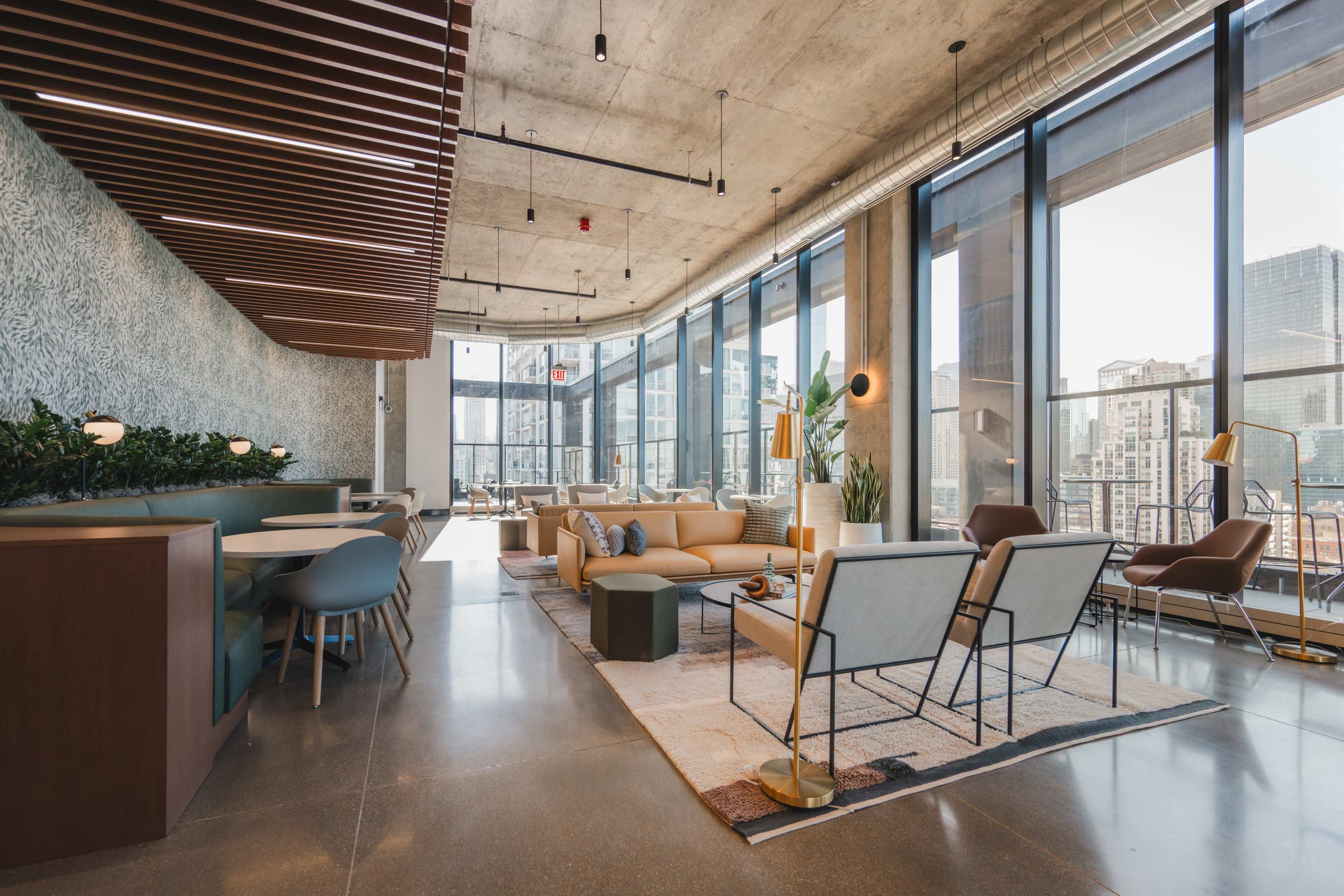 A modern lounge area features large windows that offer a view of the city skyline, with comfortable seating, a wooden ceiling structure, and a mix of plants and decorative elements.