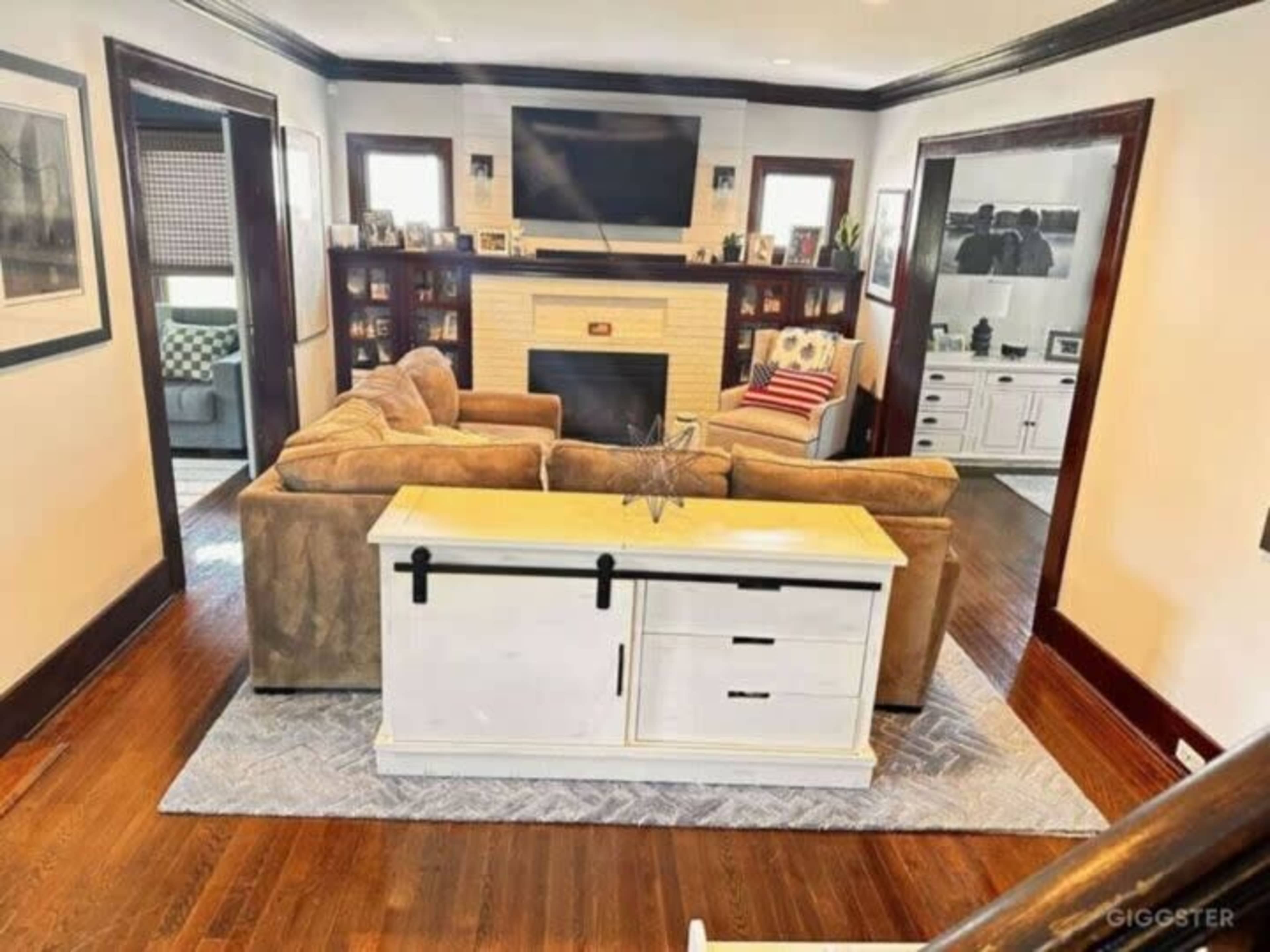 A living room with a large sectional sofa, a television mounted above a white fireplace, and a coffee table in the center.