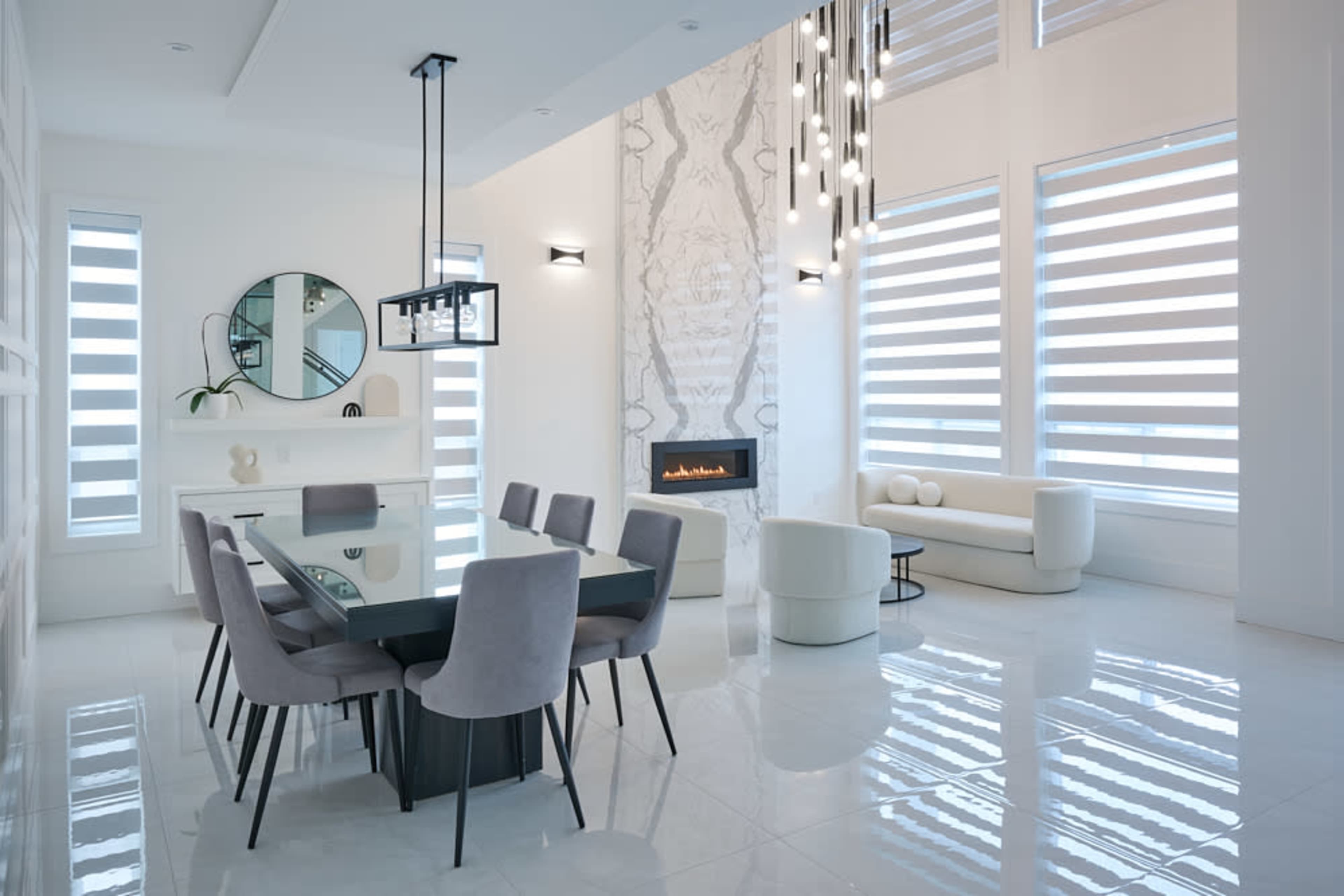 A modern interior features a dining area with a glass table surrounded by upholstered chairs, a sleek fireplace, and a minimalist seating arrangement in the adjacent lounge.