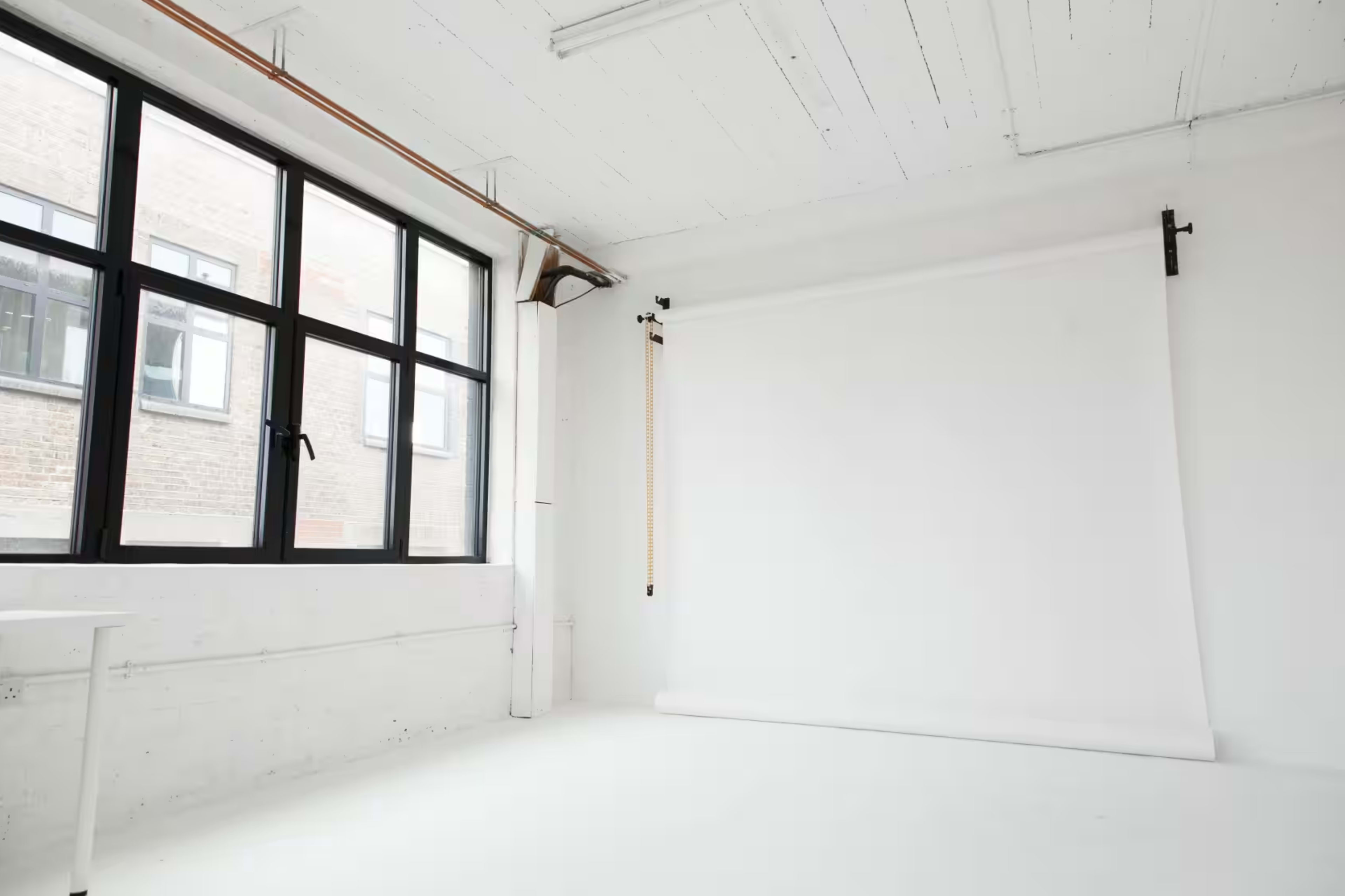 A bright, empty studio space with large windows and a white backdrop on a roll.