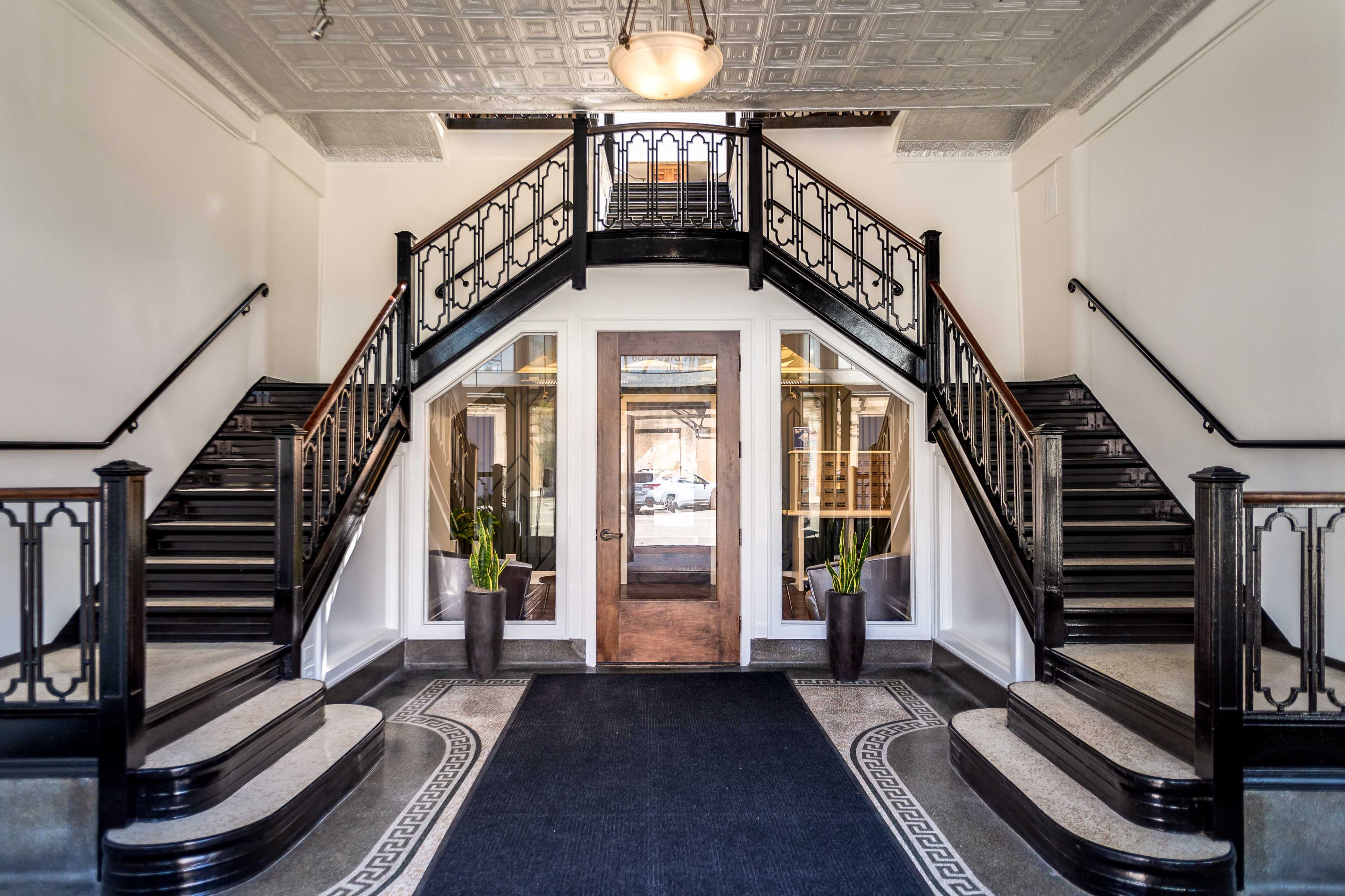 A symmetrical entrance hall with a wooden door flanked by dual curved staircases leading to an upper level.