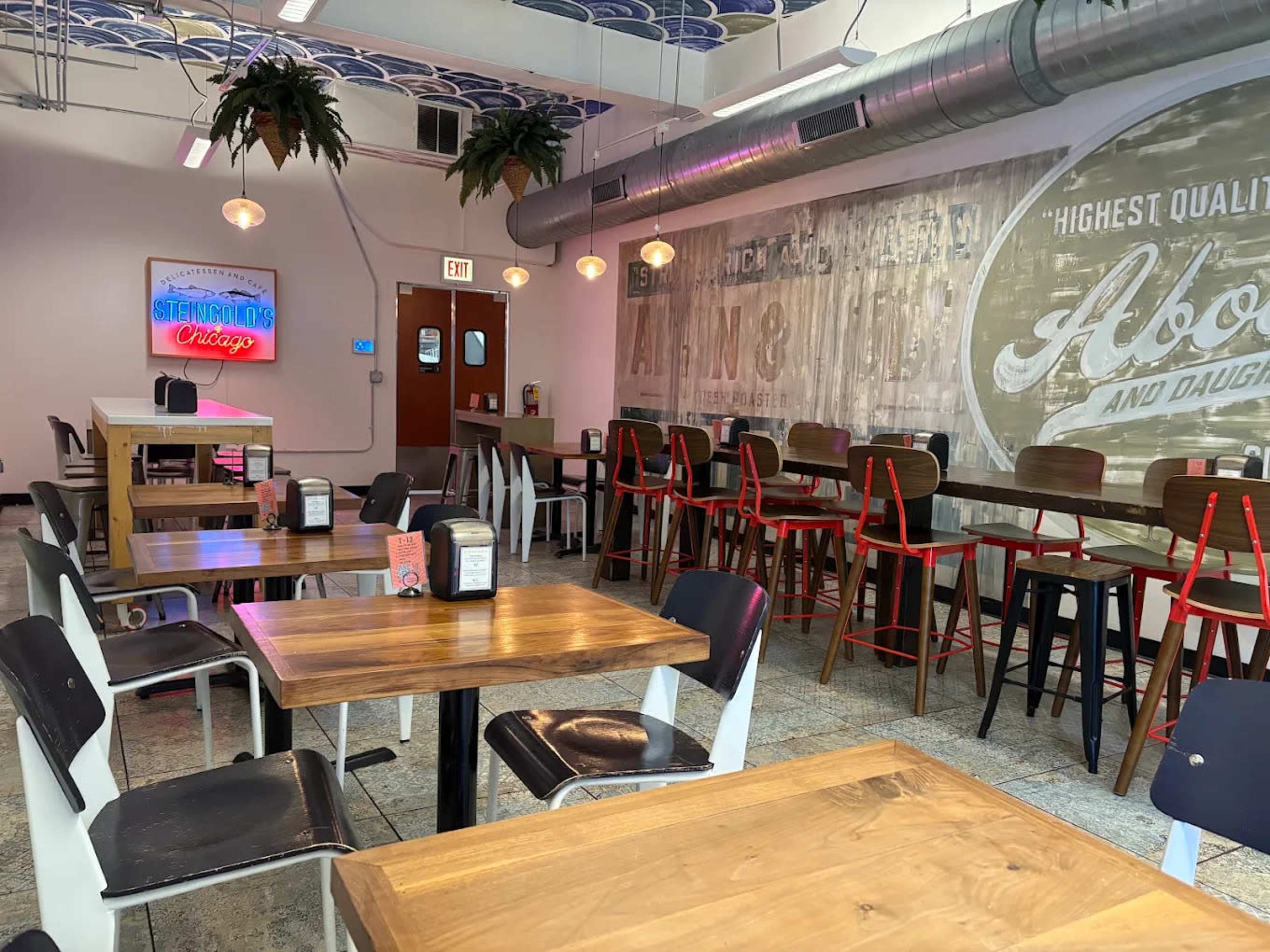 The image shows an indoor dining area with wooden tables, a mix of seating options, and decorative neon signs on the walls.