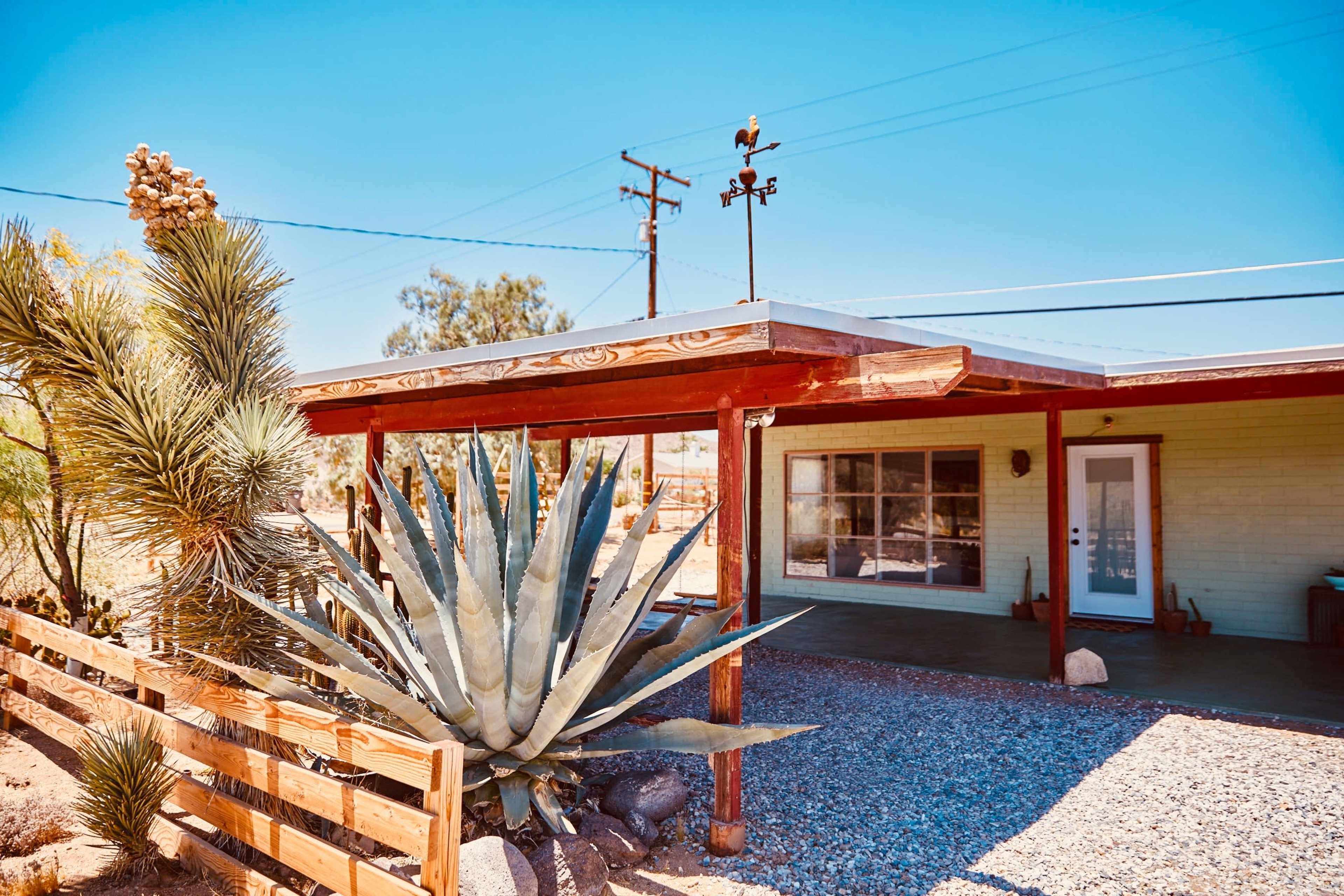 The image shows a single-story house with a porch and a large agave plant in the foreground, set in a desert landscape.