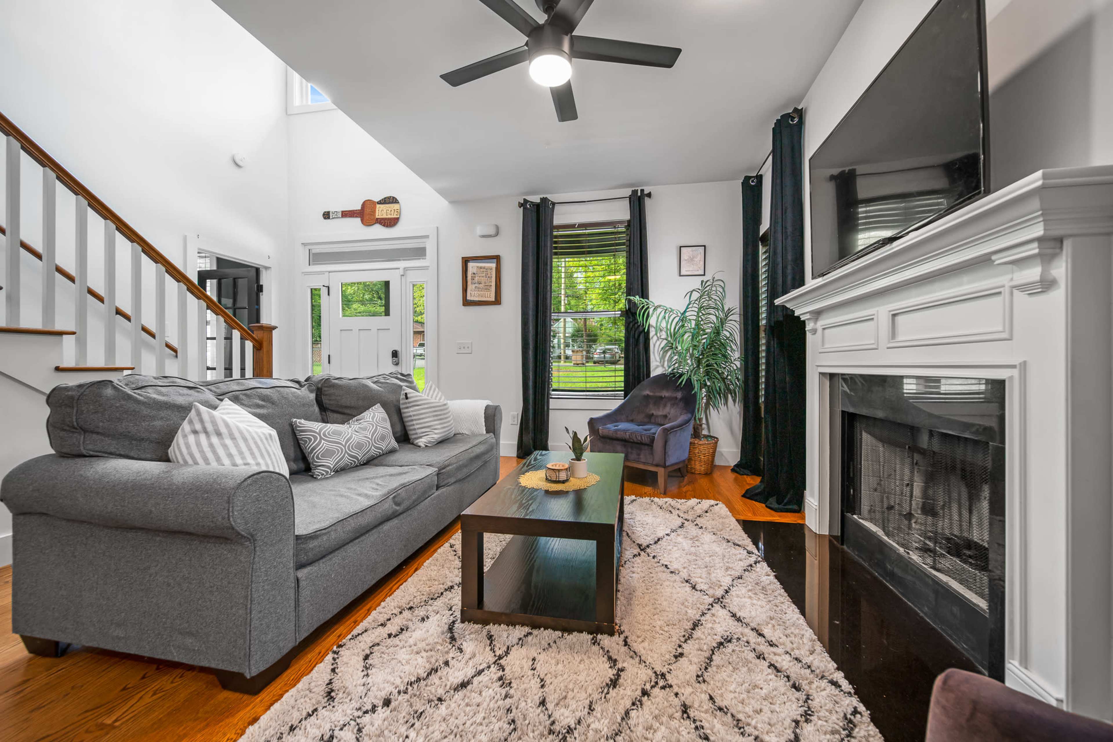 A modern living room features a gray sofa, a coffee table, and a fireplace, with large windows providing natural light.