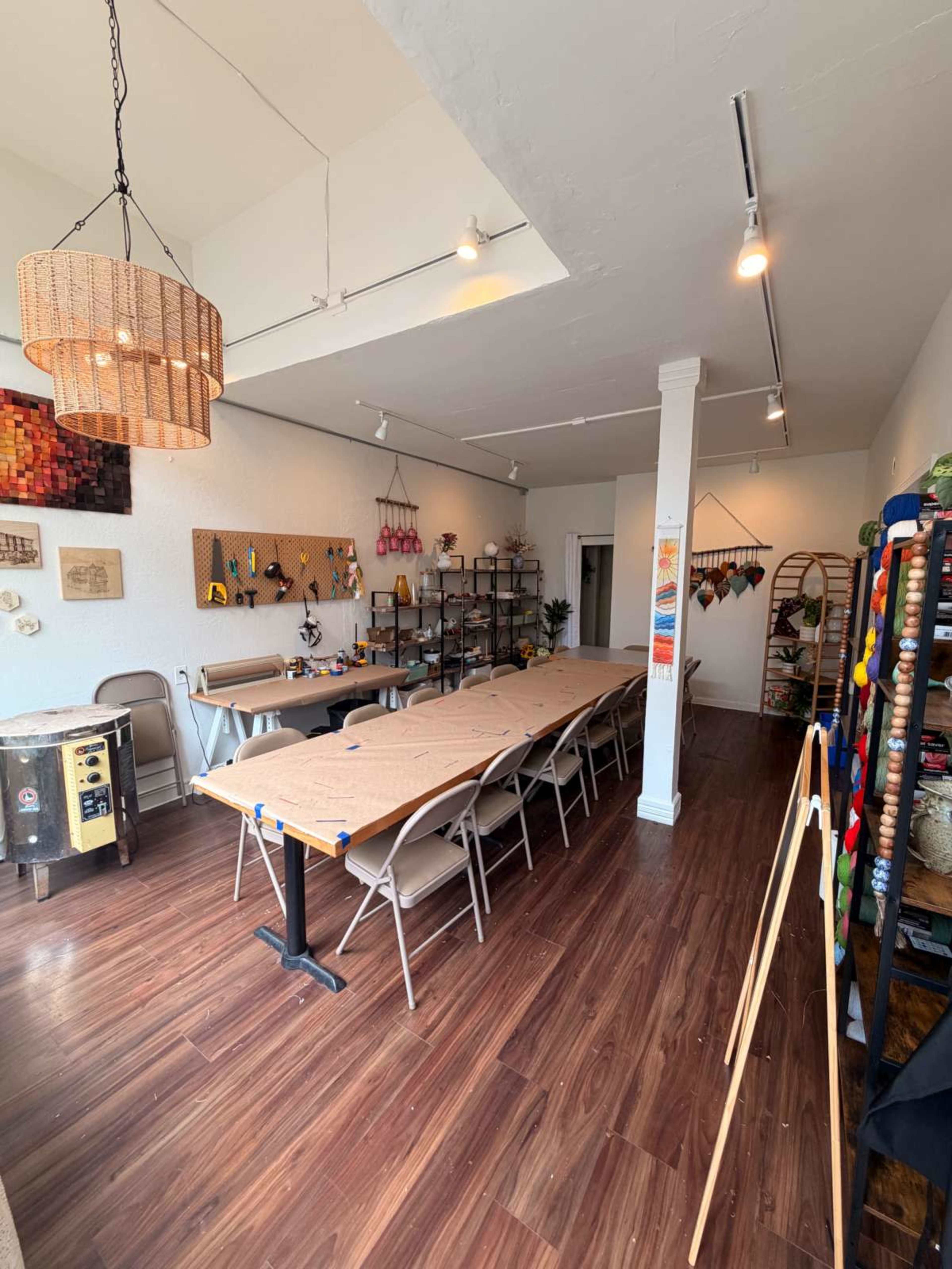 The image shows a well-lit room with a long table surrounded by chairs, a hanging chandelier, and shelves featuring various decorative items.