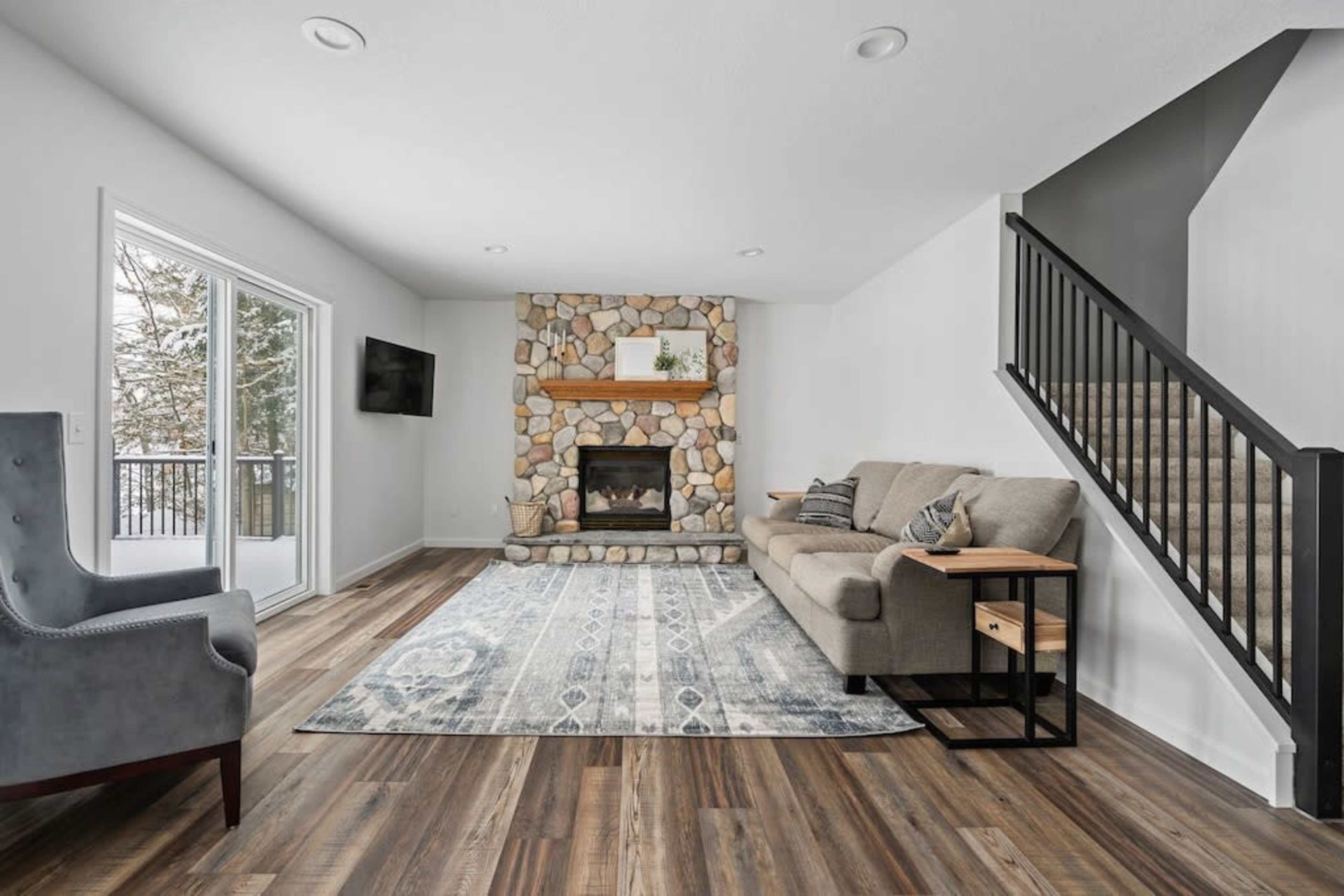 The living room features a stone fireplace, a gray sofa, and access to a balcony through sliding glass doors.