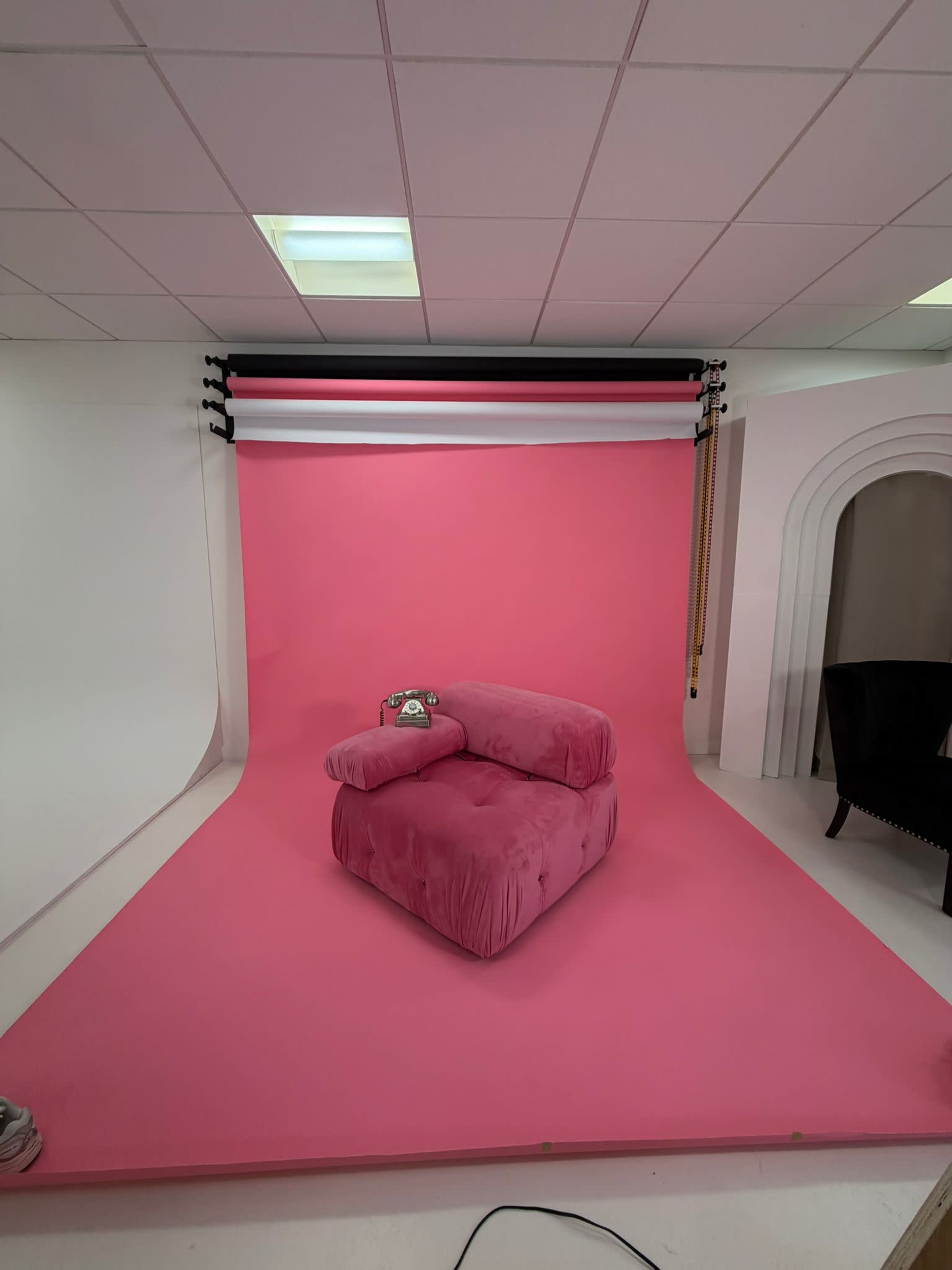 The image shows a pink velvet couch positioned against a bright pink backdrop in a photography studio.
