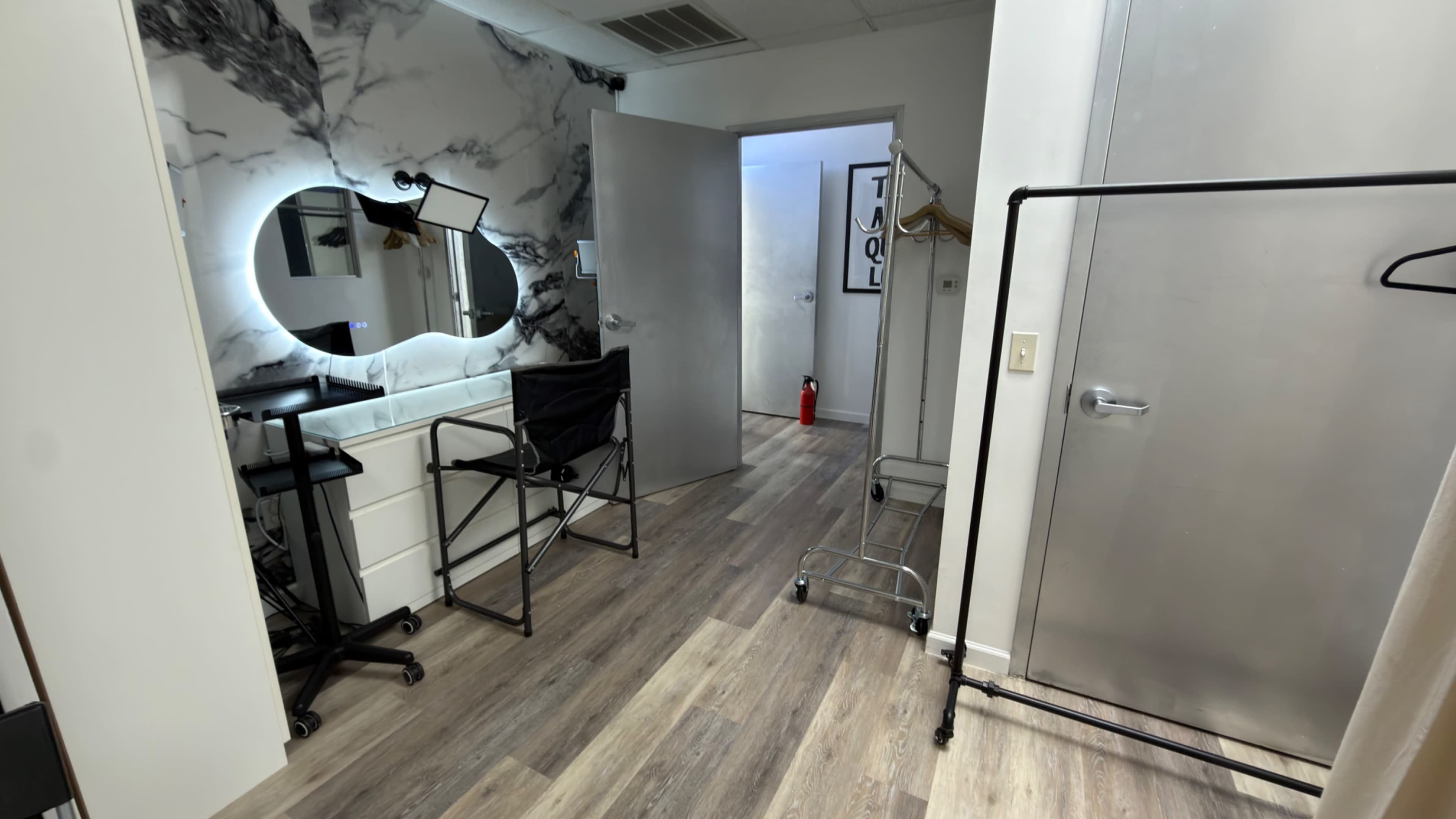 The image shows a well-lit dressing room featuring a large mirror, vanity, and clothing racks against a backdrop of marble-patterned walls.