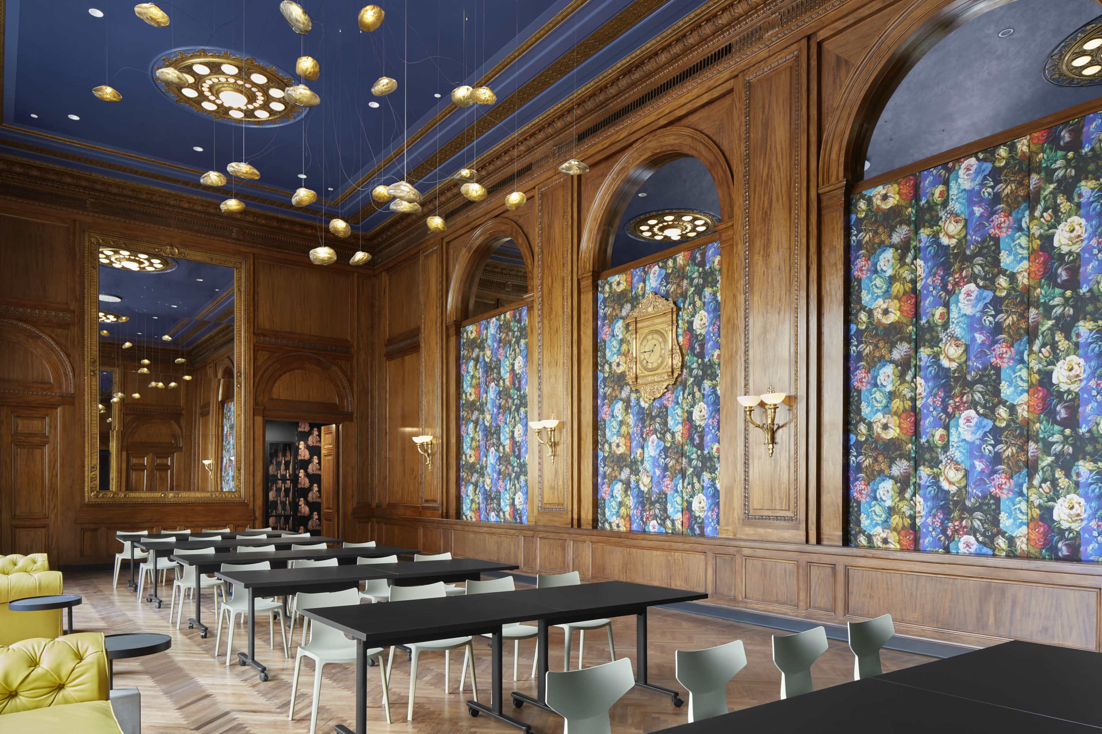 A spacious room with wooden paneling, floral wallpaper, ornate ceiling lights, and multiple tables arranged for an event.
