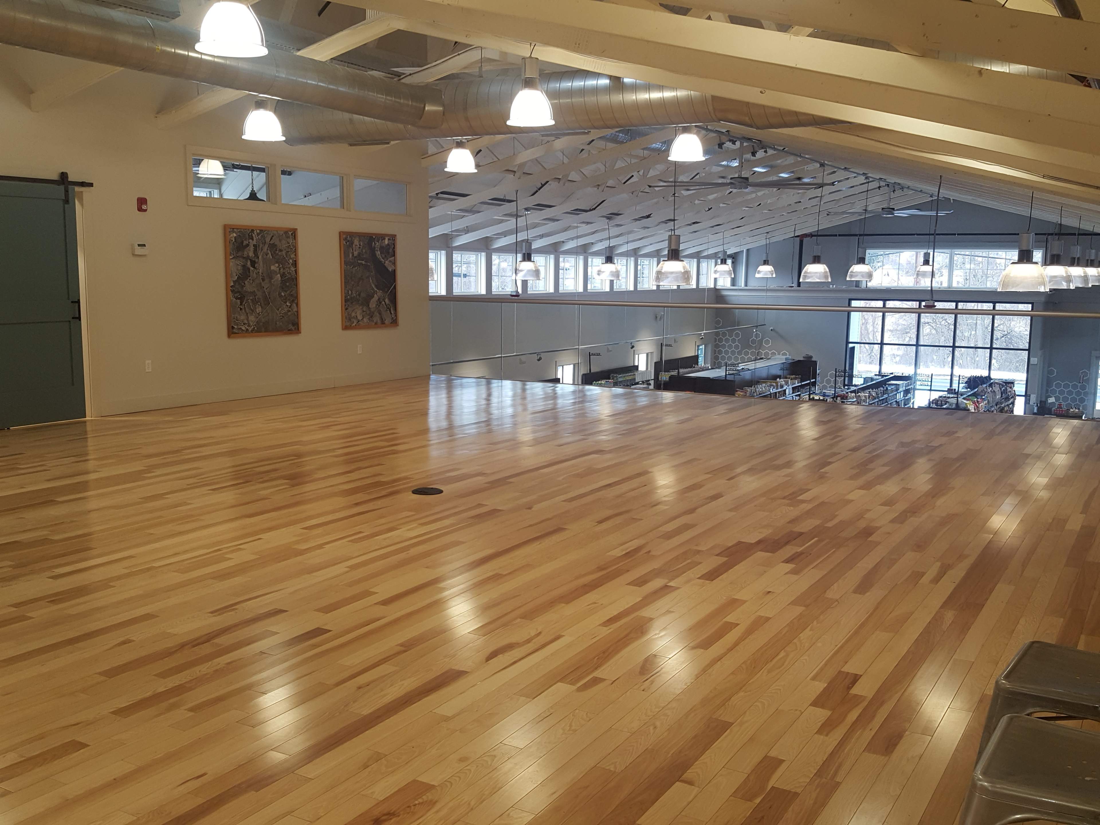 A spacious wooden floor in a well-lit room with vaulted ceilings and large windows in the background.