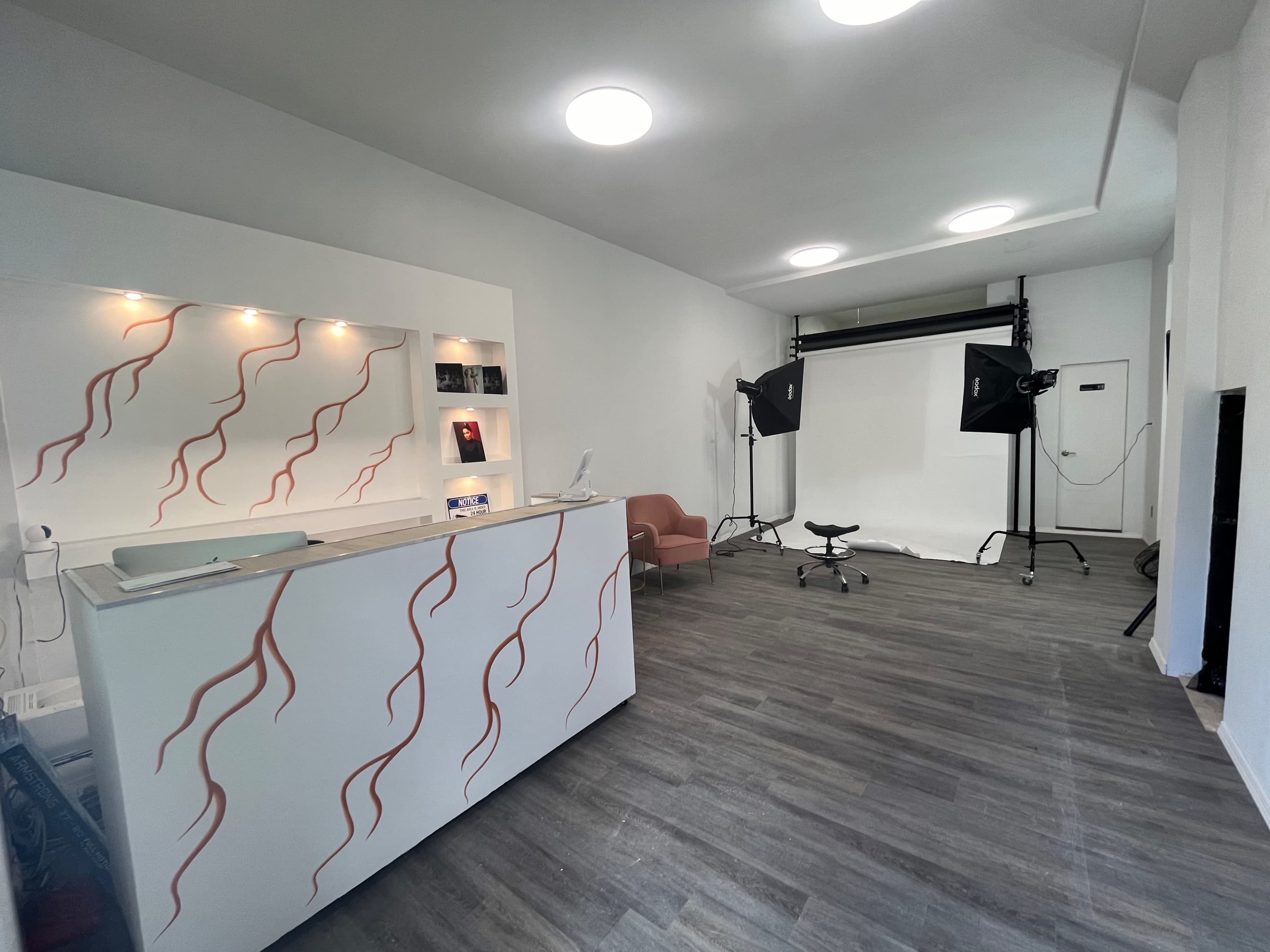 A minimalist interior with a reception area featuring a white counter and a backdrop setup for photography on the right side of the room.