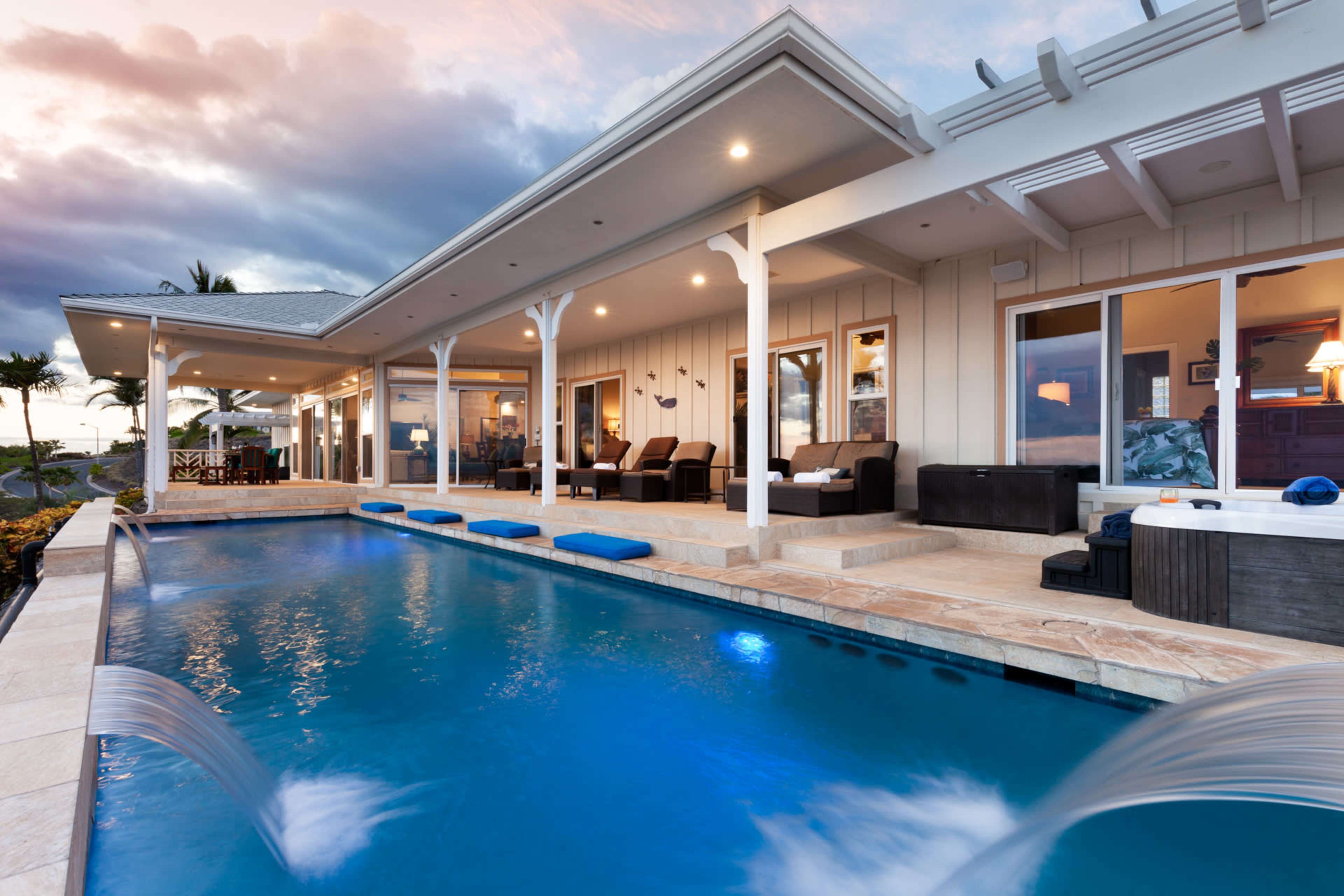 The image shows a modern single-story home with a pool in the foreground and a patio area, set against a backdrop of clouds.