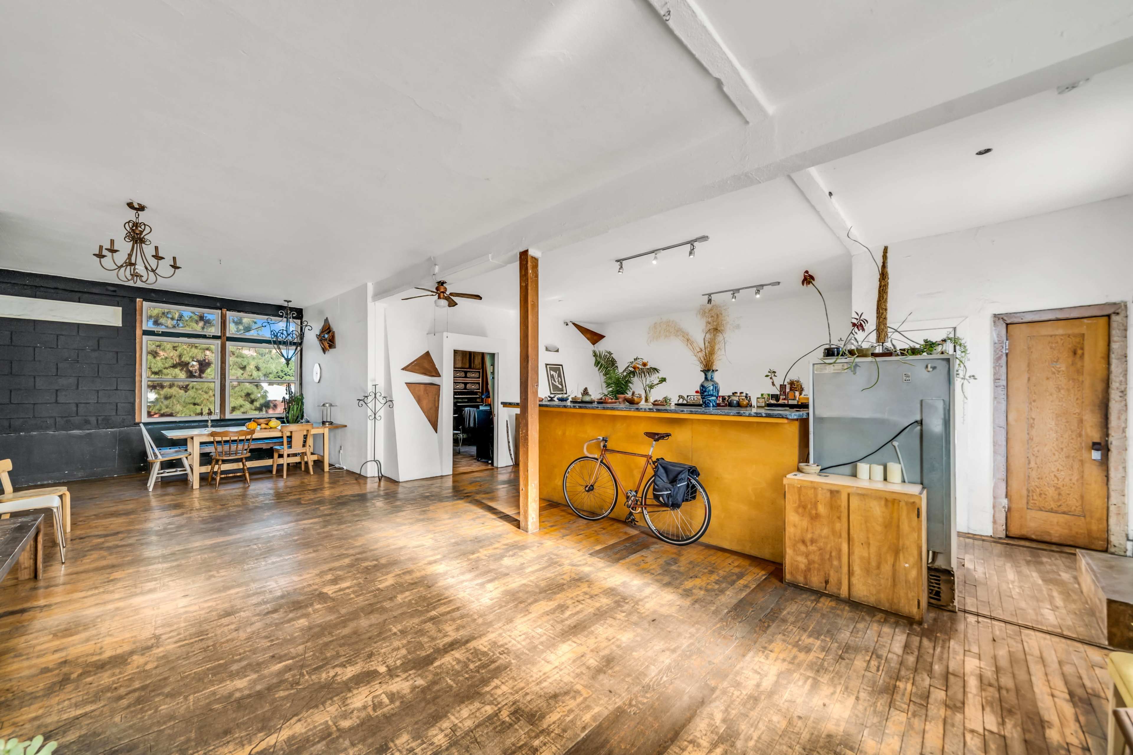 An open layout of a spacious, well-lit room featuring wooden floors, a kitchen area with a bike, and a dining space with a table.