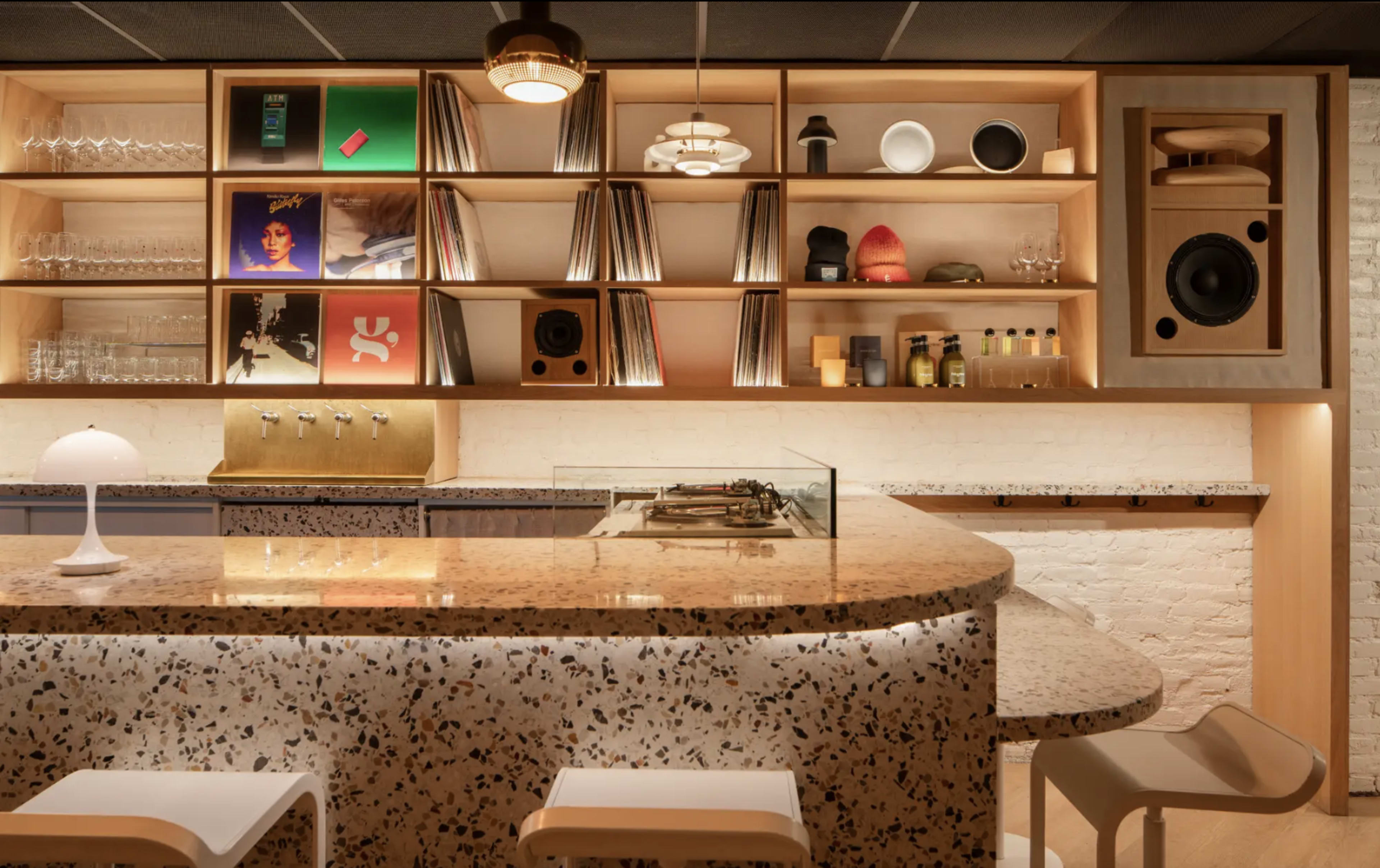 A modern kitchen with a speckled countertop, wooden shelving displaying vinyl records and various kitchen items, and a seating area with white chairs.