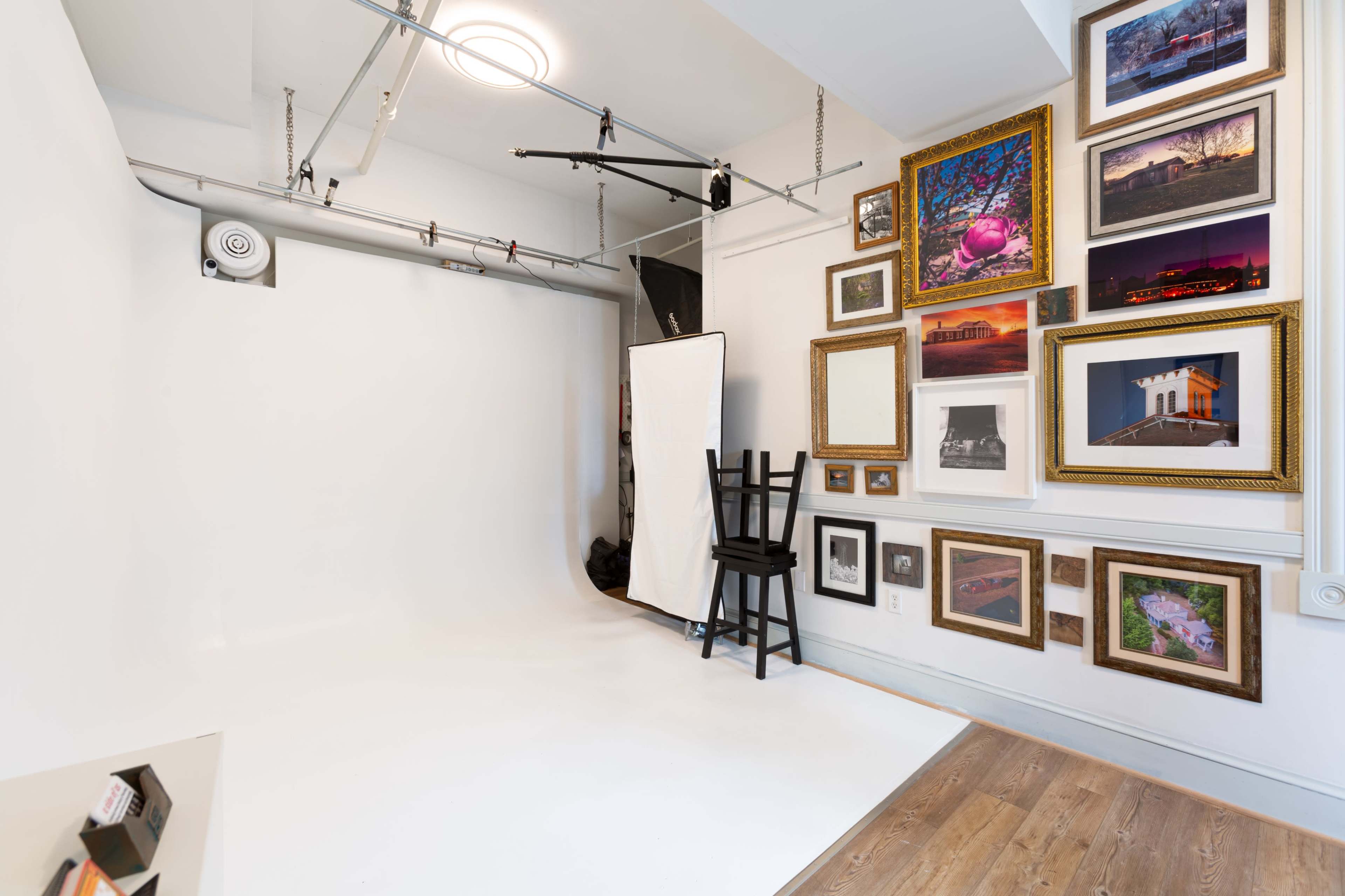 A photography studio with a blank white backdrop and a wall adorned with various framed photographs and artwork.