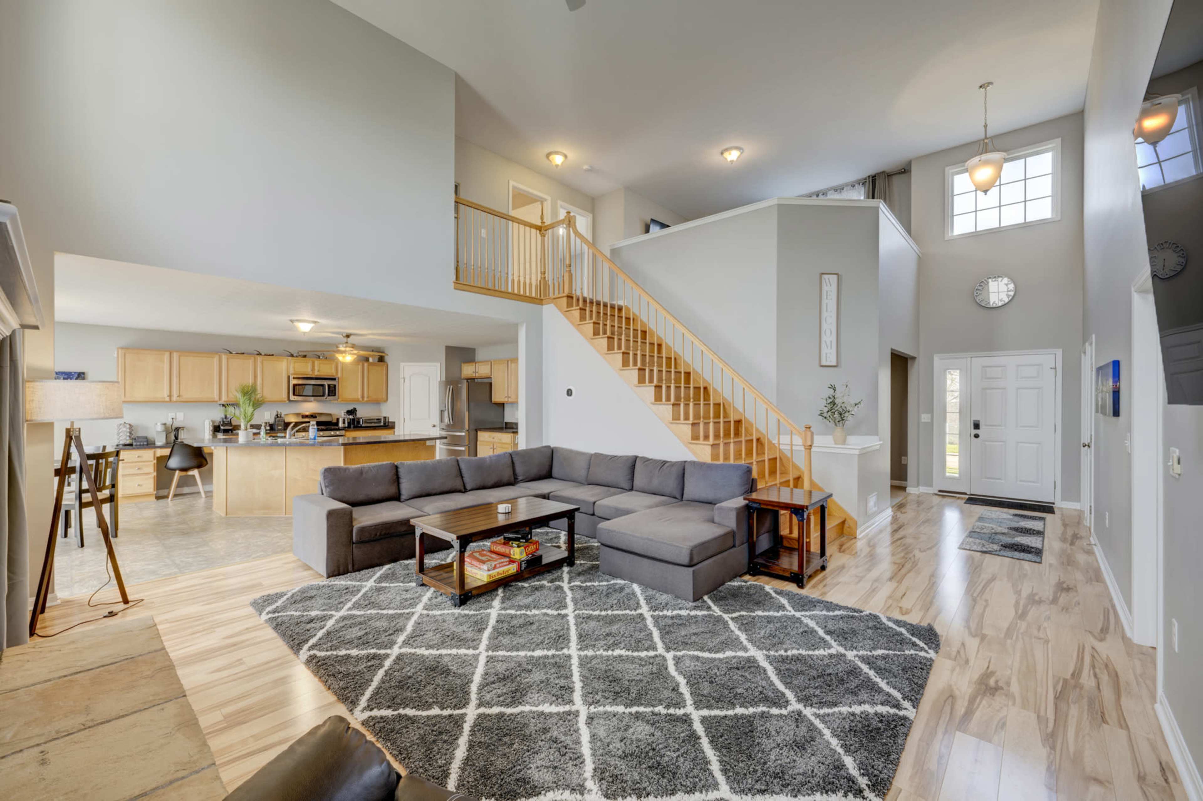 A modern living area with a sectional sofa, coffee table, and a staircase leading to an upper level, adjacent to an open kitchen and dining area.