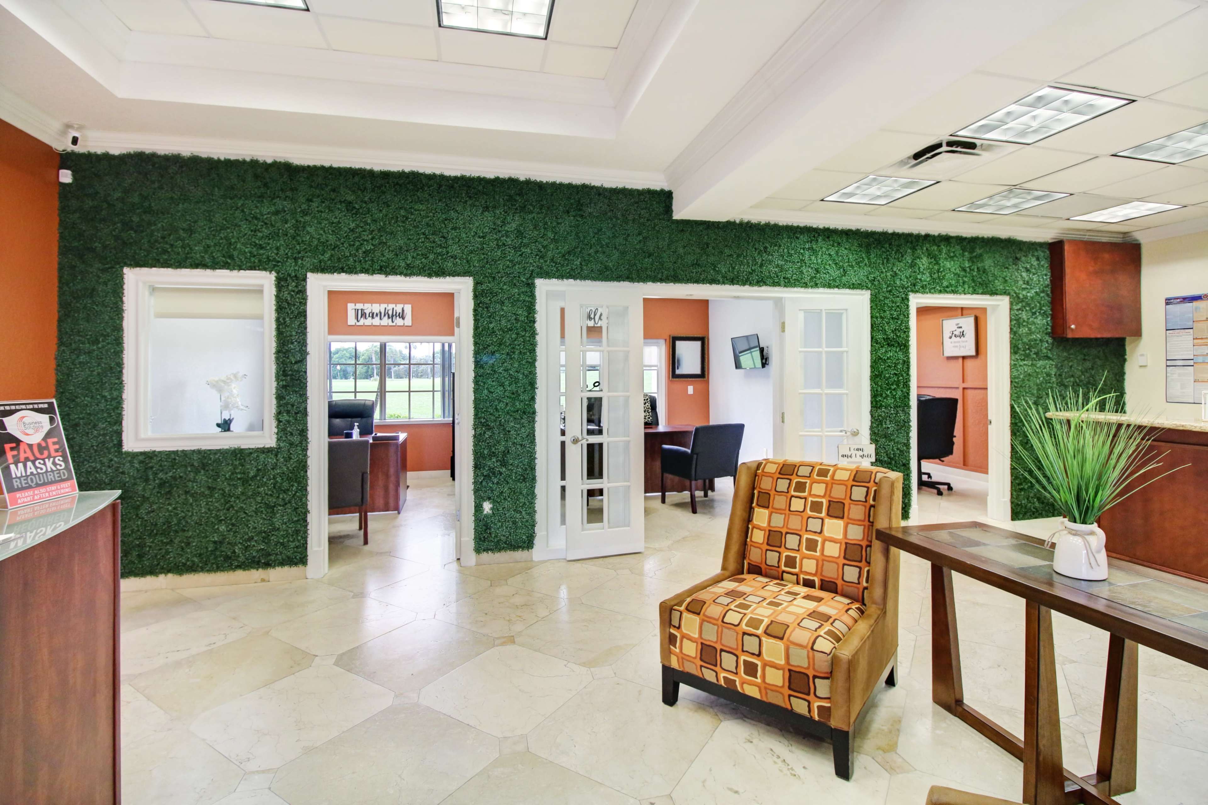 The image shows an office reception area featuring a green wall, two glass doors leading to additional rooms, and a seating area with a patterned chair.