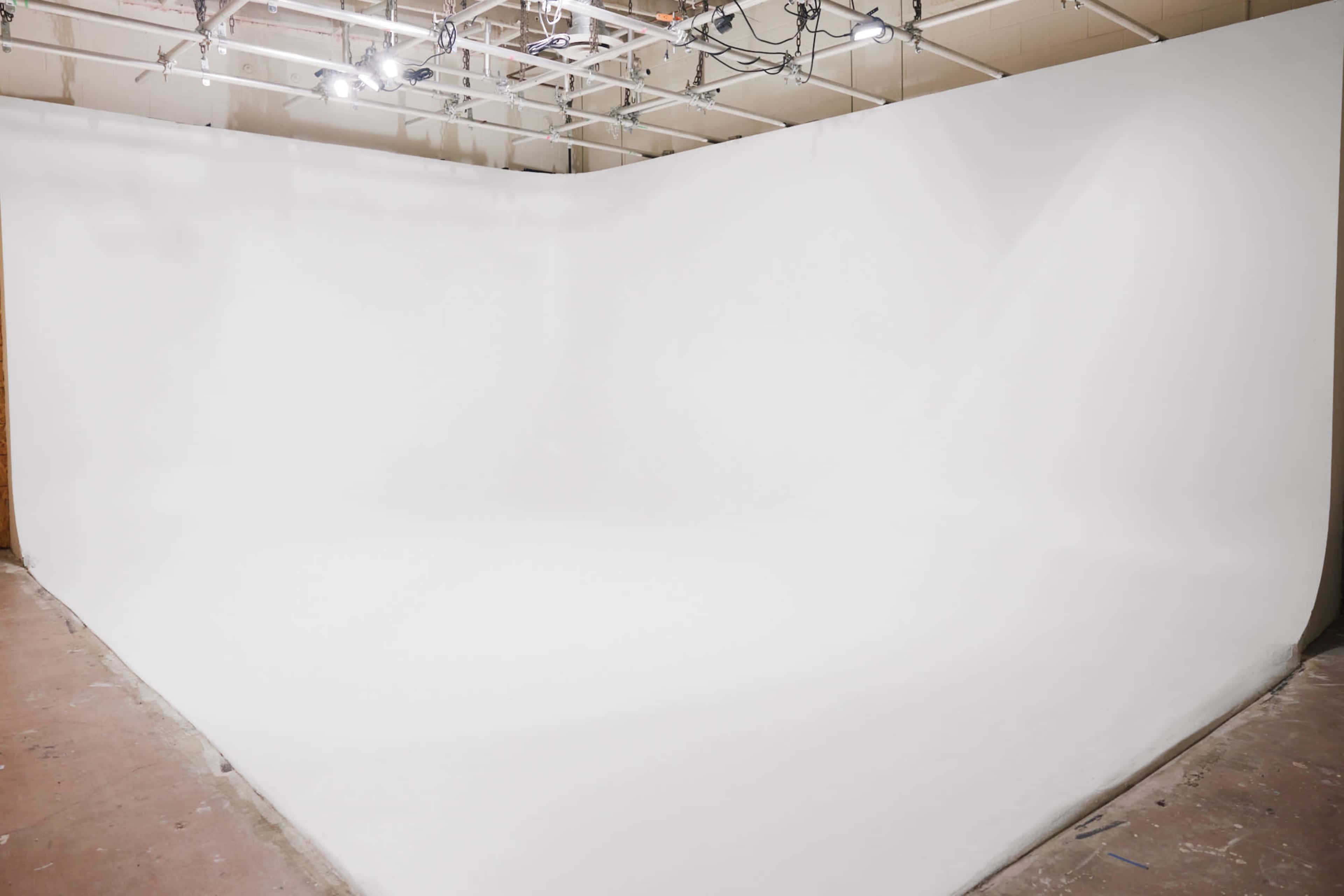 The image shows a spacious photography studio with a seamless white backdrop and overhead lighting.
