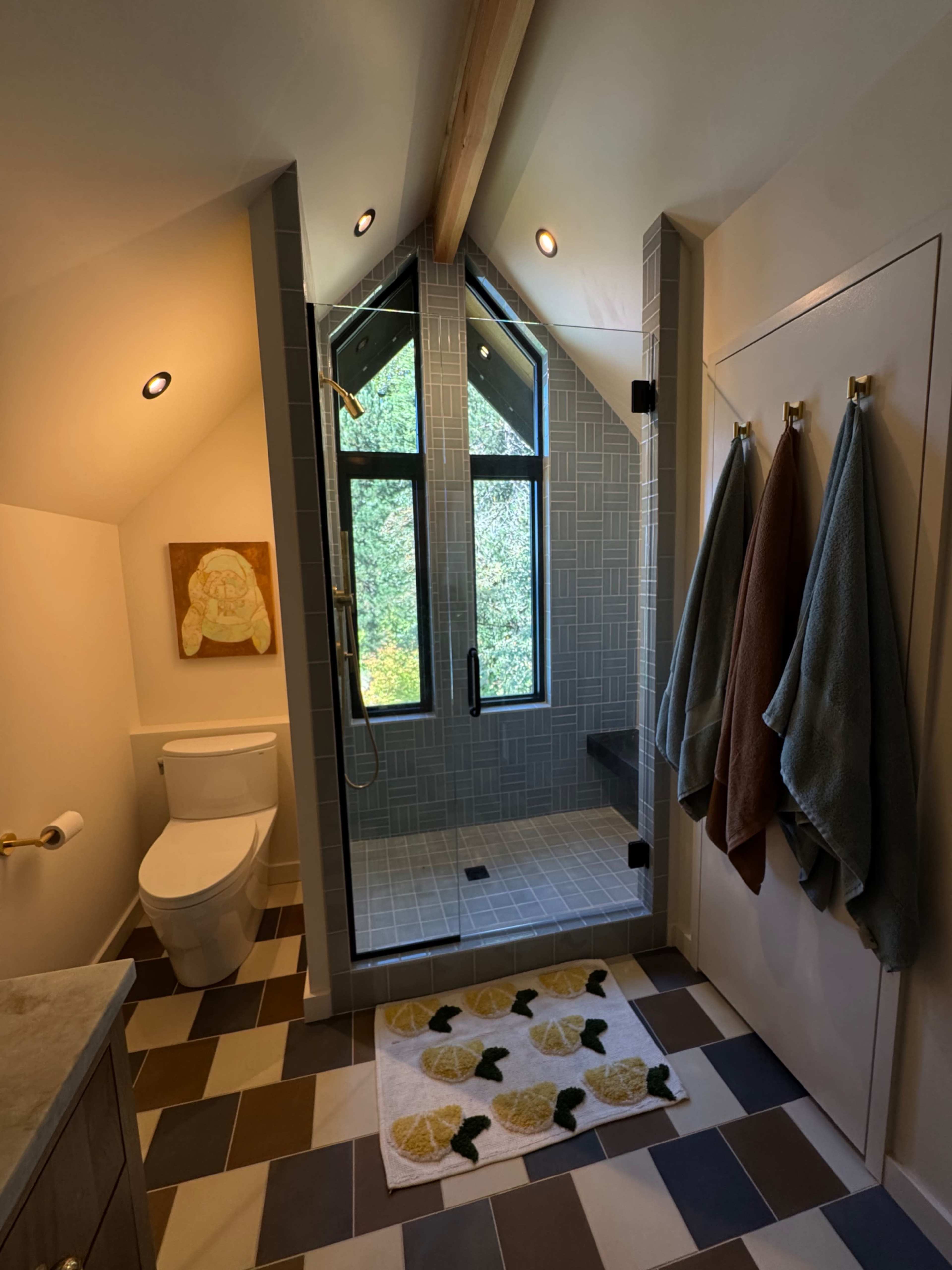 The image shows a modern bathroom featuring a tiled shower area, a toilet, and a decorative rug on the floor.