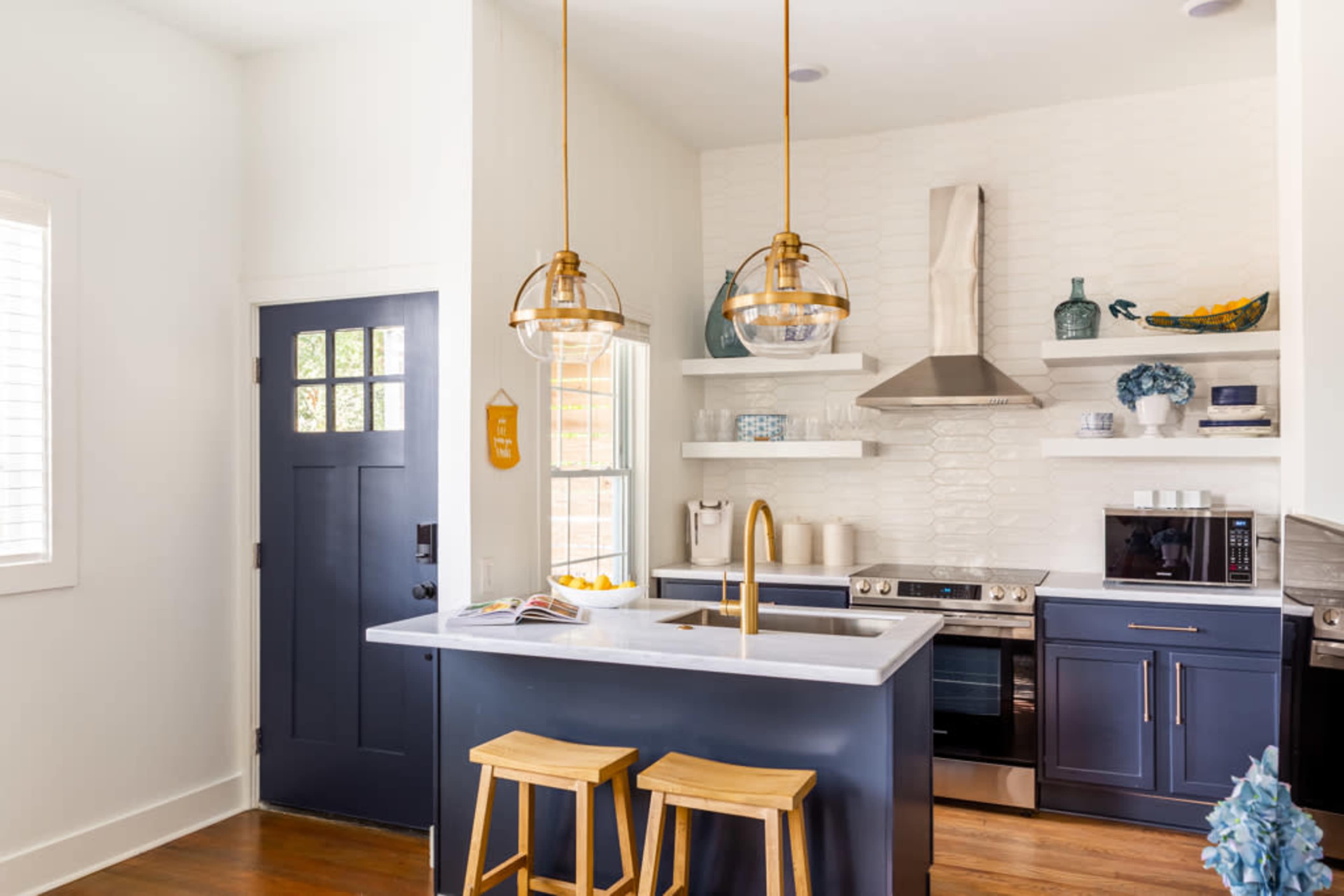 A modern kitchen features blue cabinetry, a large island with bar stools, and gold pendant lights above the sink, alongside stainless steel appliances.