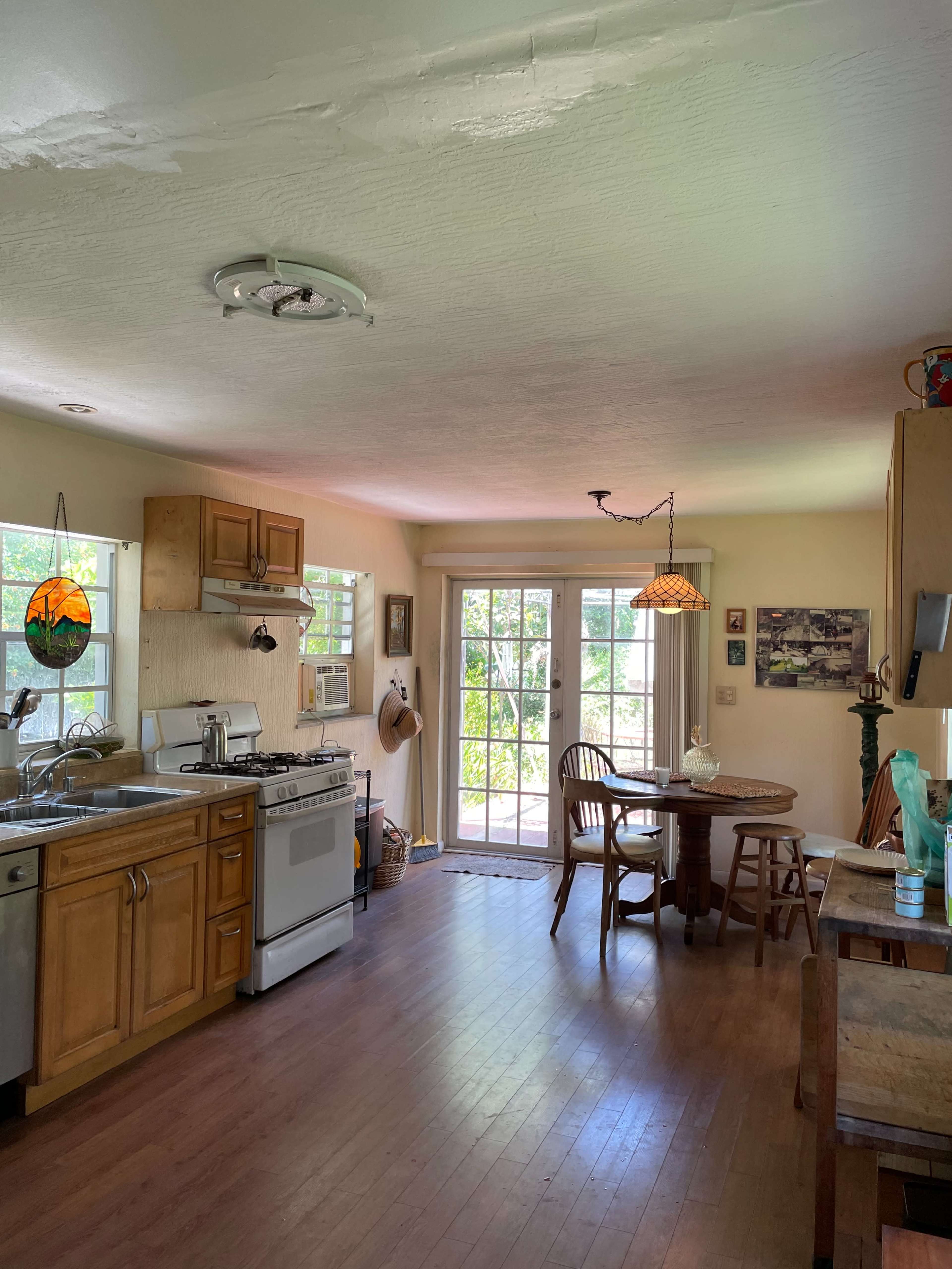 The kitchen features wooden cabinets, a gas stove, and a dining table near a glass door that opens to the outside.