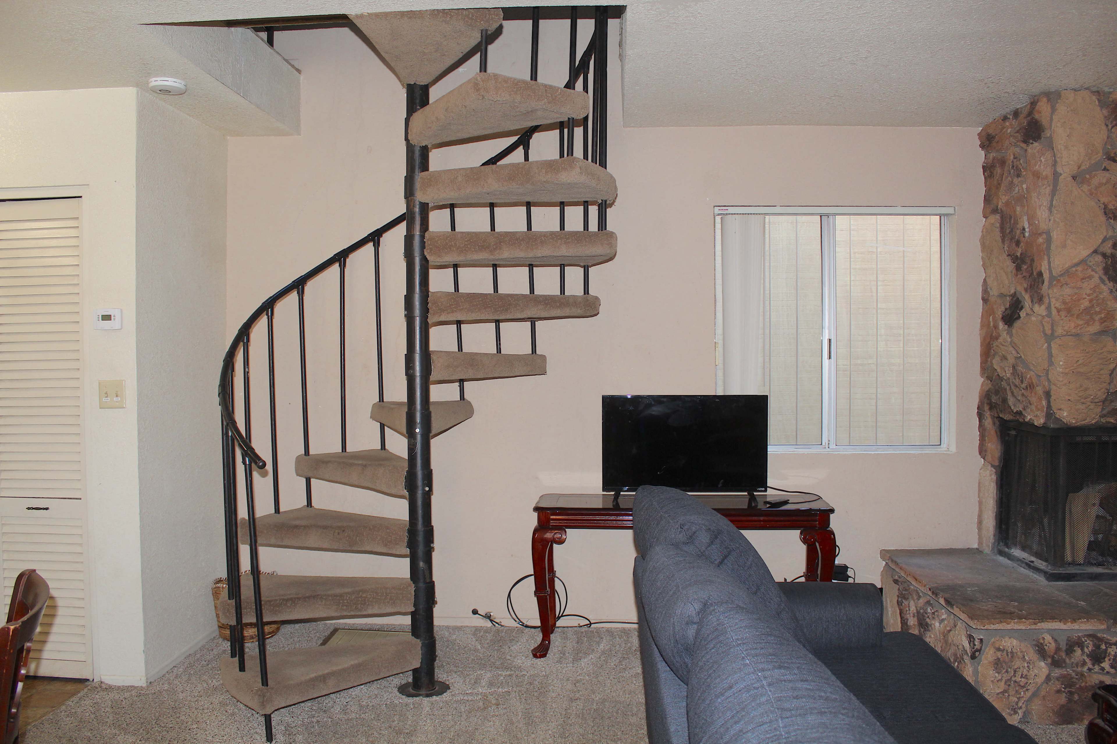 A spiral staircase leads from the lower level to the upper area of a room with a couch and a television.