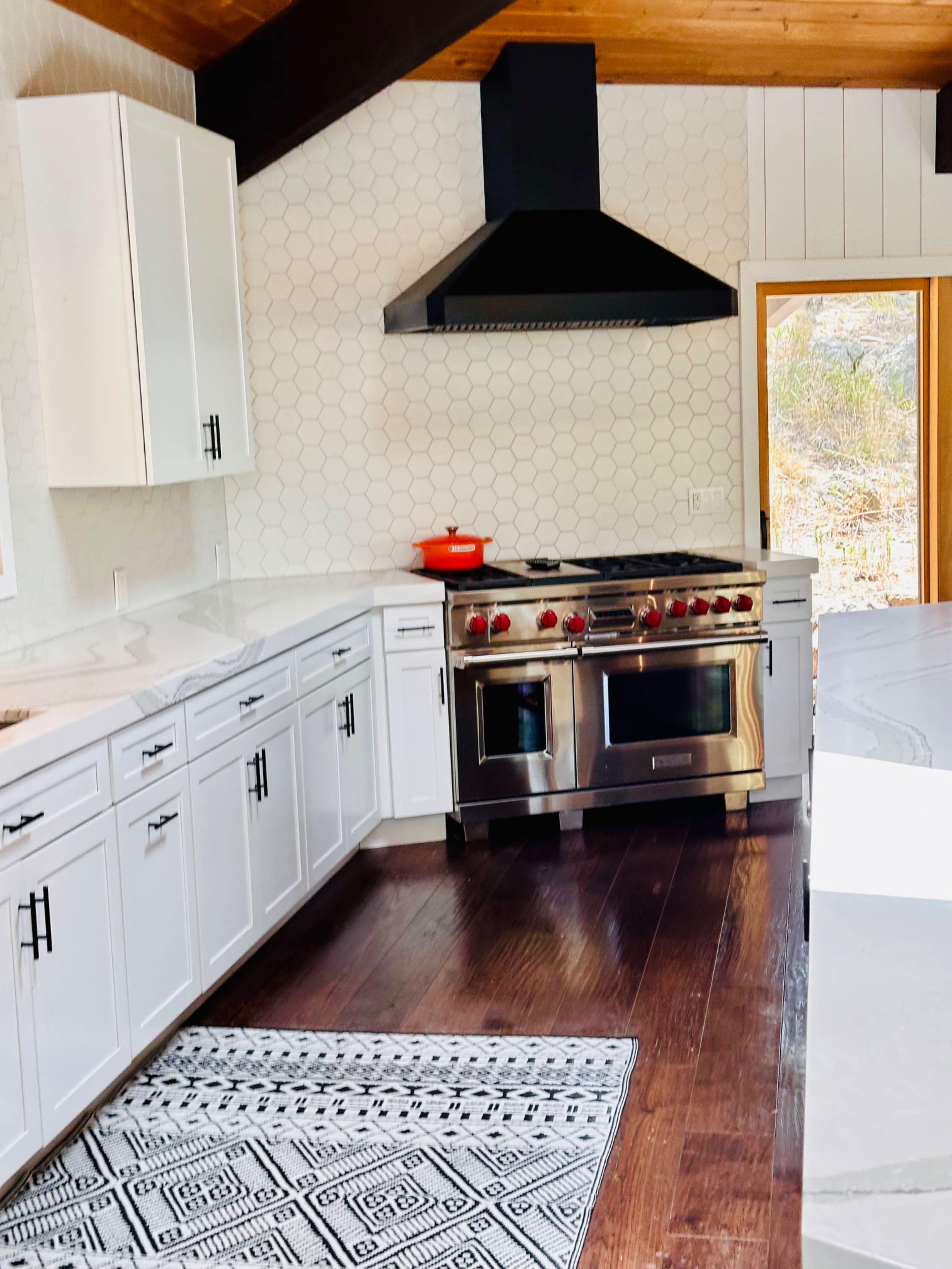 A modern kitchen features white cabinetry, a stainless steel gas range, and a large window with natural light.