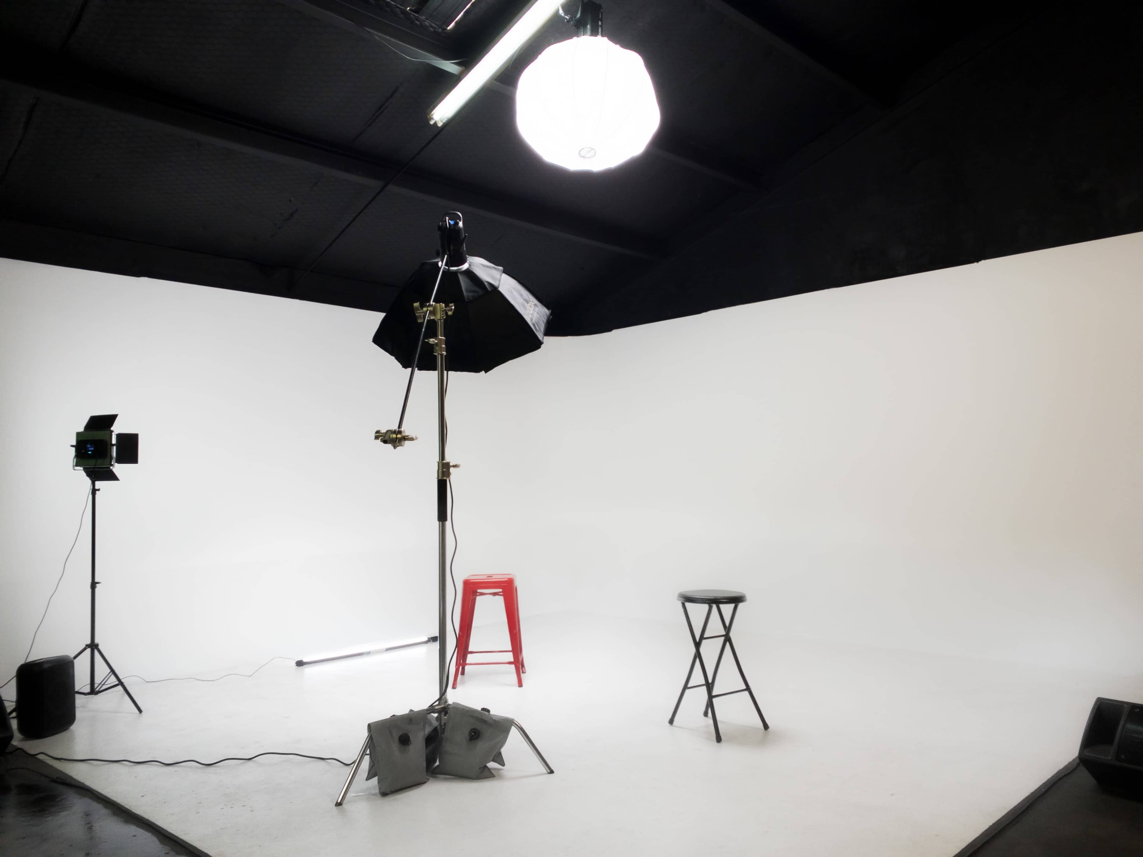 A minimalistic photography studio with two stools, a softbox light, and a spotlight on a white backdrop.