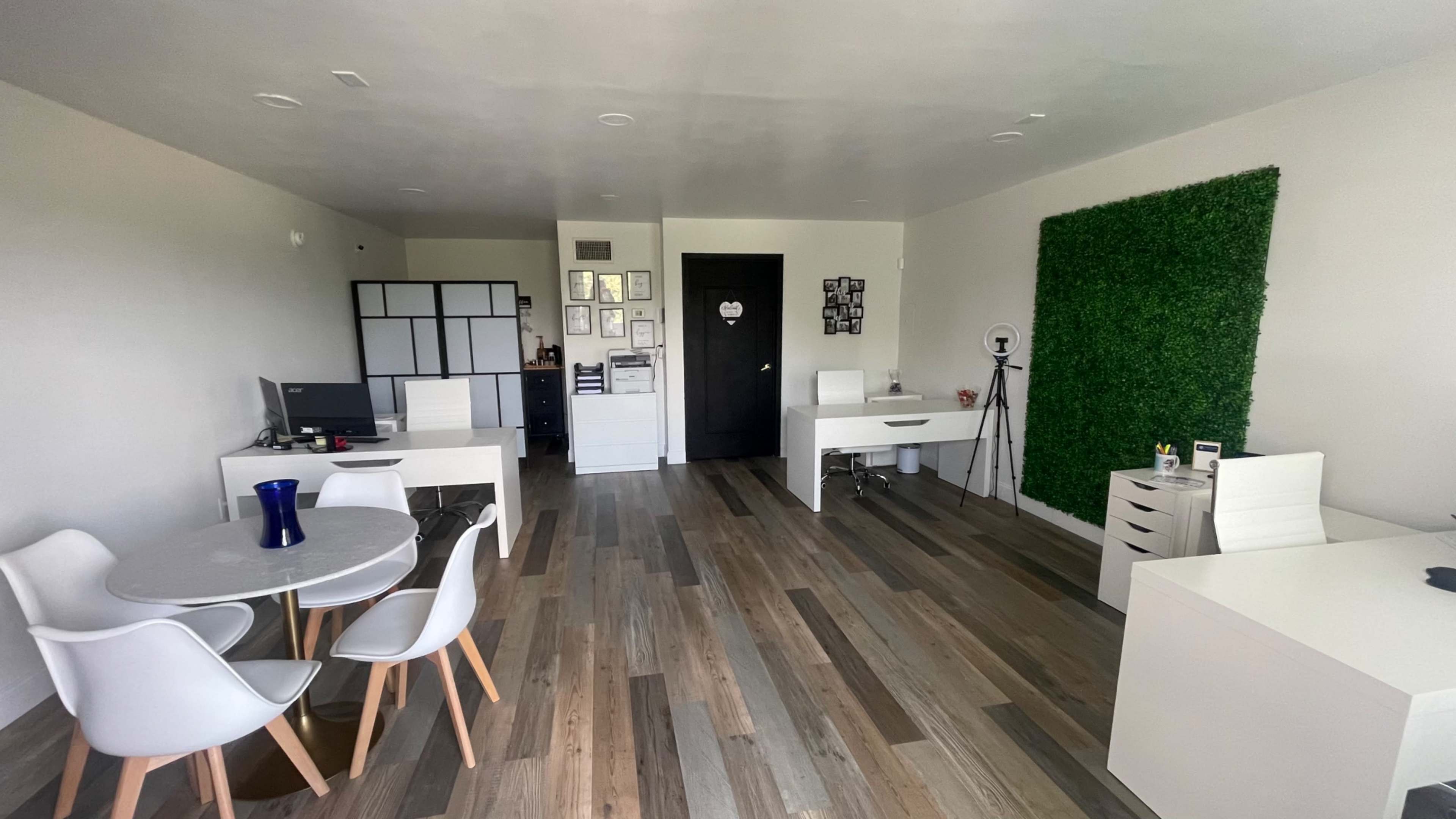 A modern office space featuring white desks, chairs, a round dining table, and a green wall accent.
