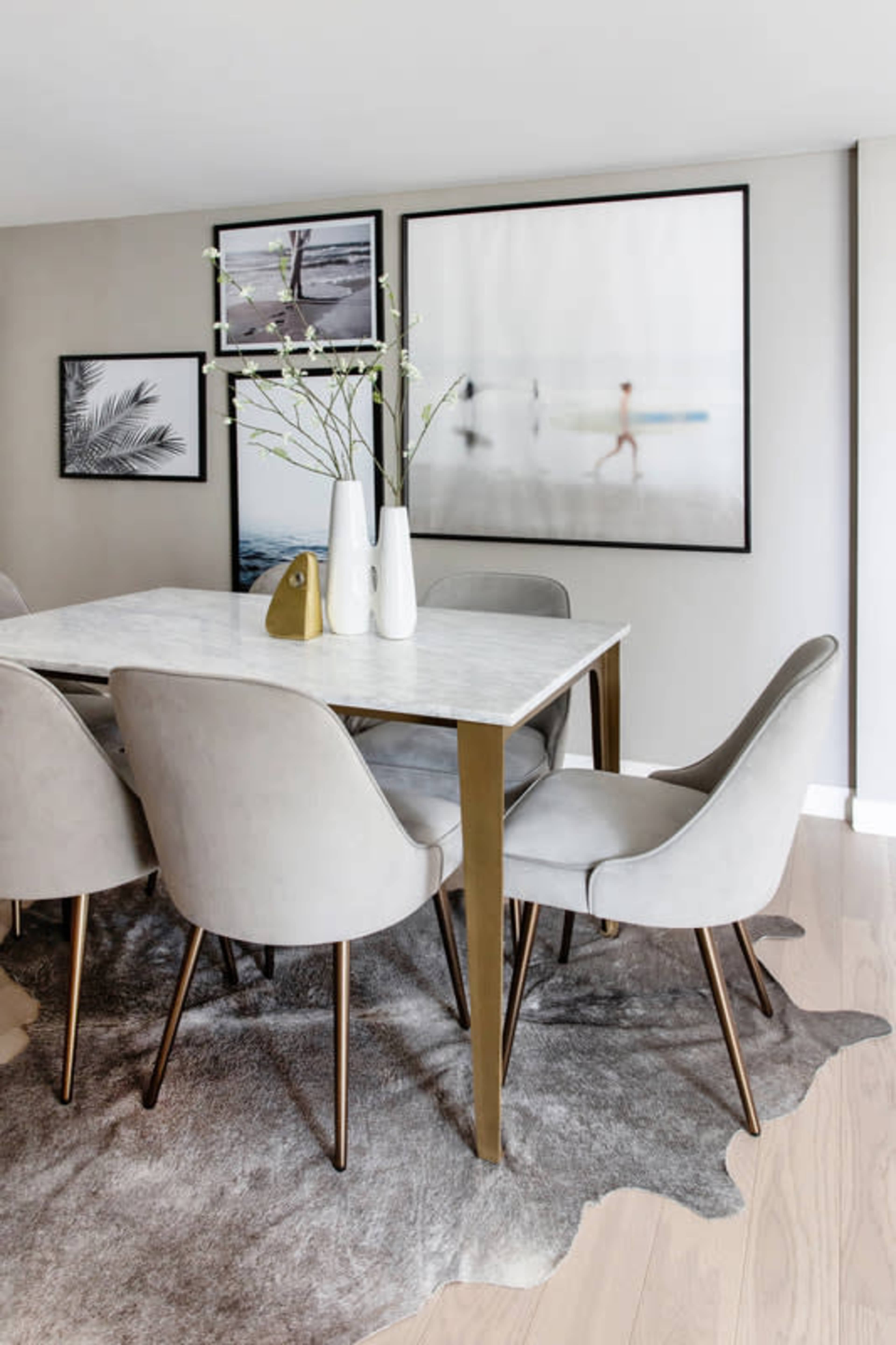 A dining area features a marble-top table surrounded by gray upholstered chairs and decorated with artwork on the walls.