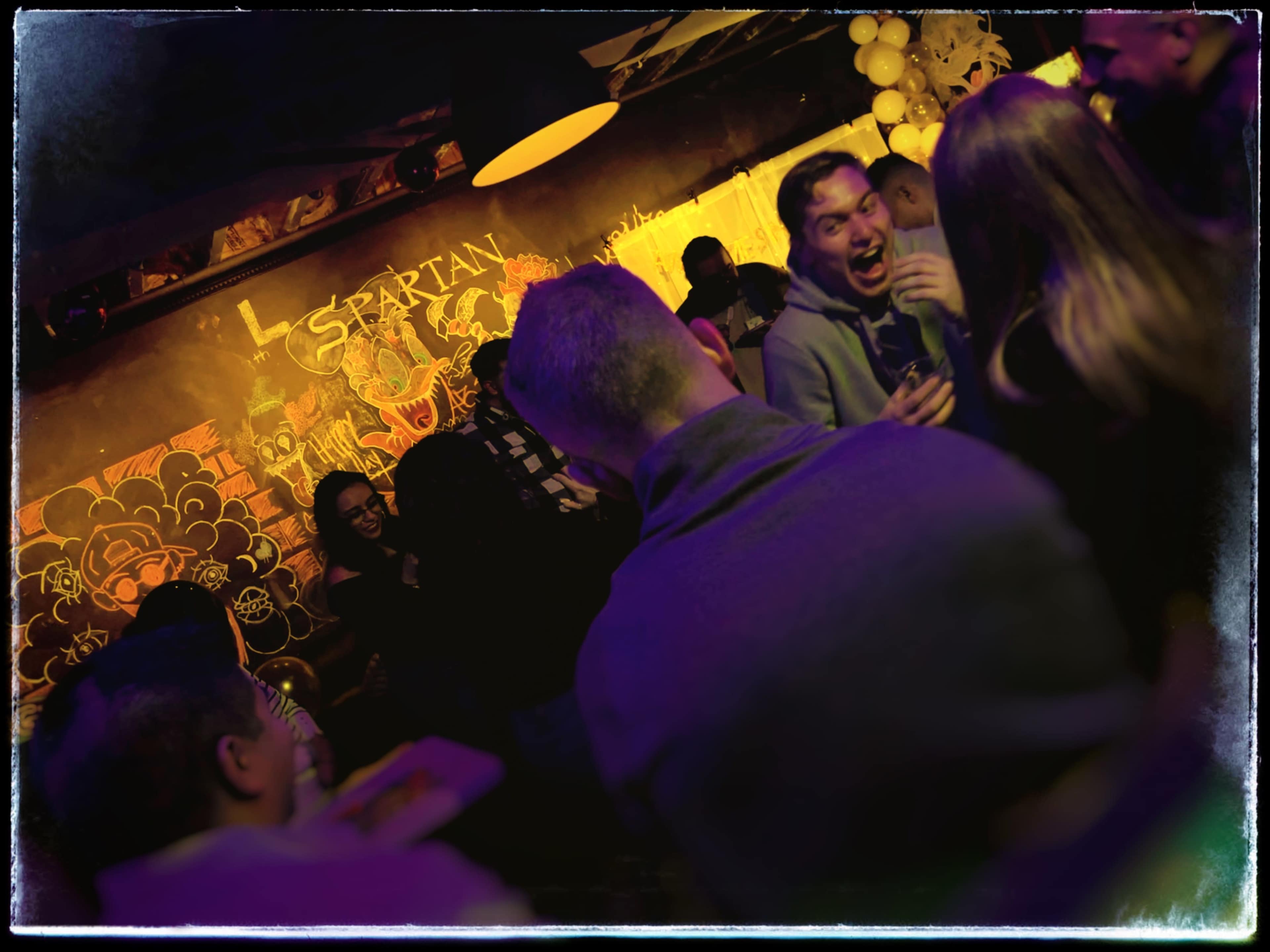 A group of people socialize in a dimly lit venue adorned with colorful murals.