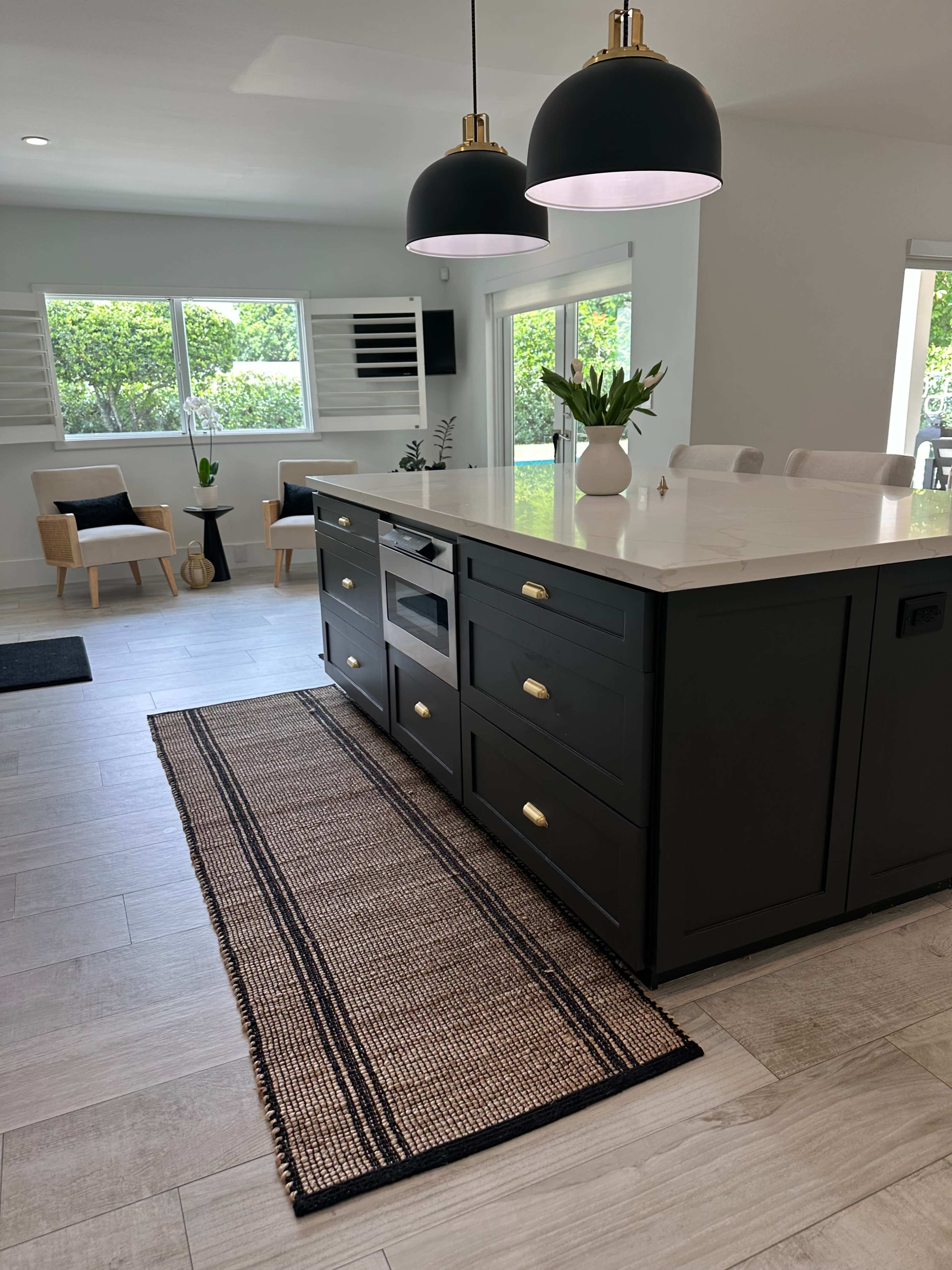 The image shows a modern kitchen with a central island, two pendant lights above it, and a woven rug on the floor.