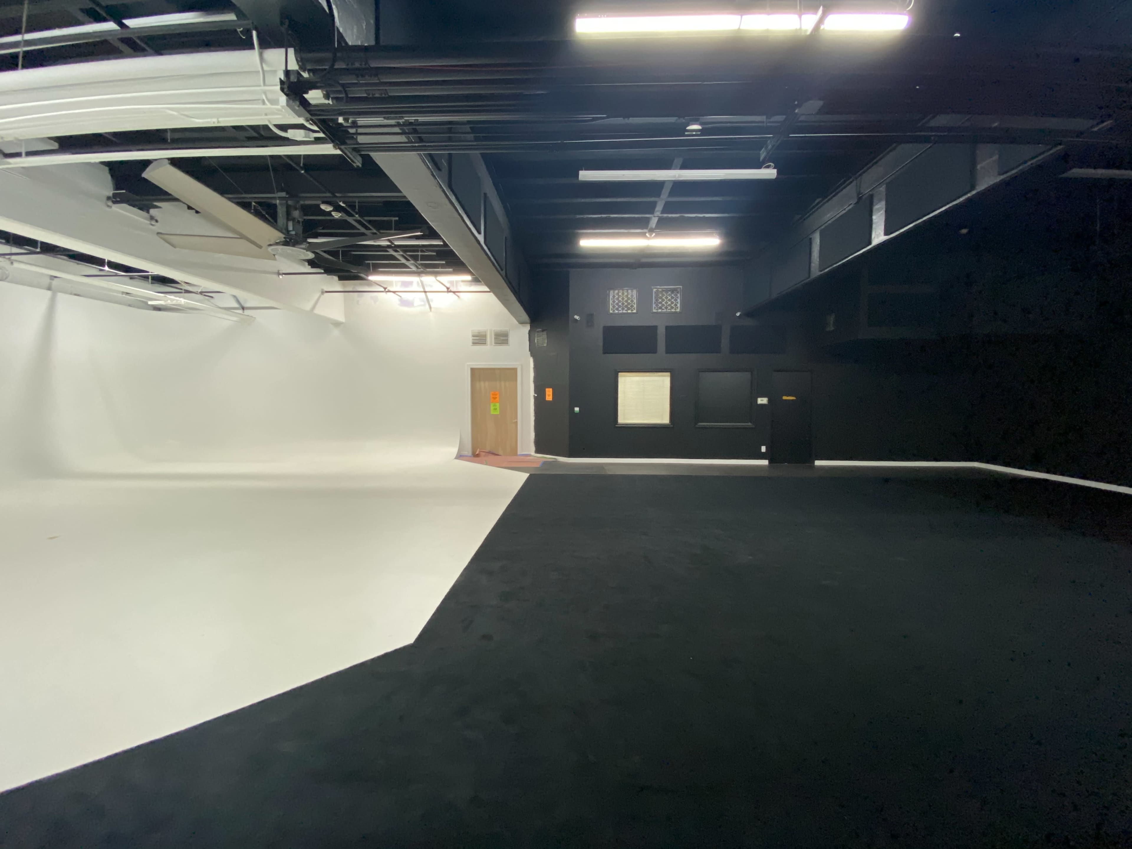 A large studio space featuring a white backdrop on one side and a black wall on the opposite side.