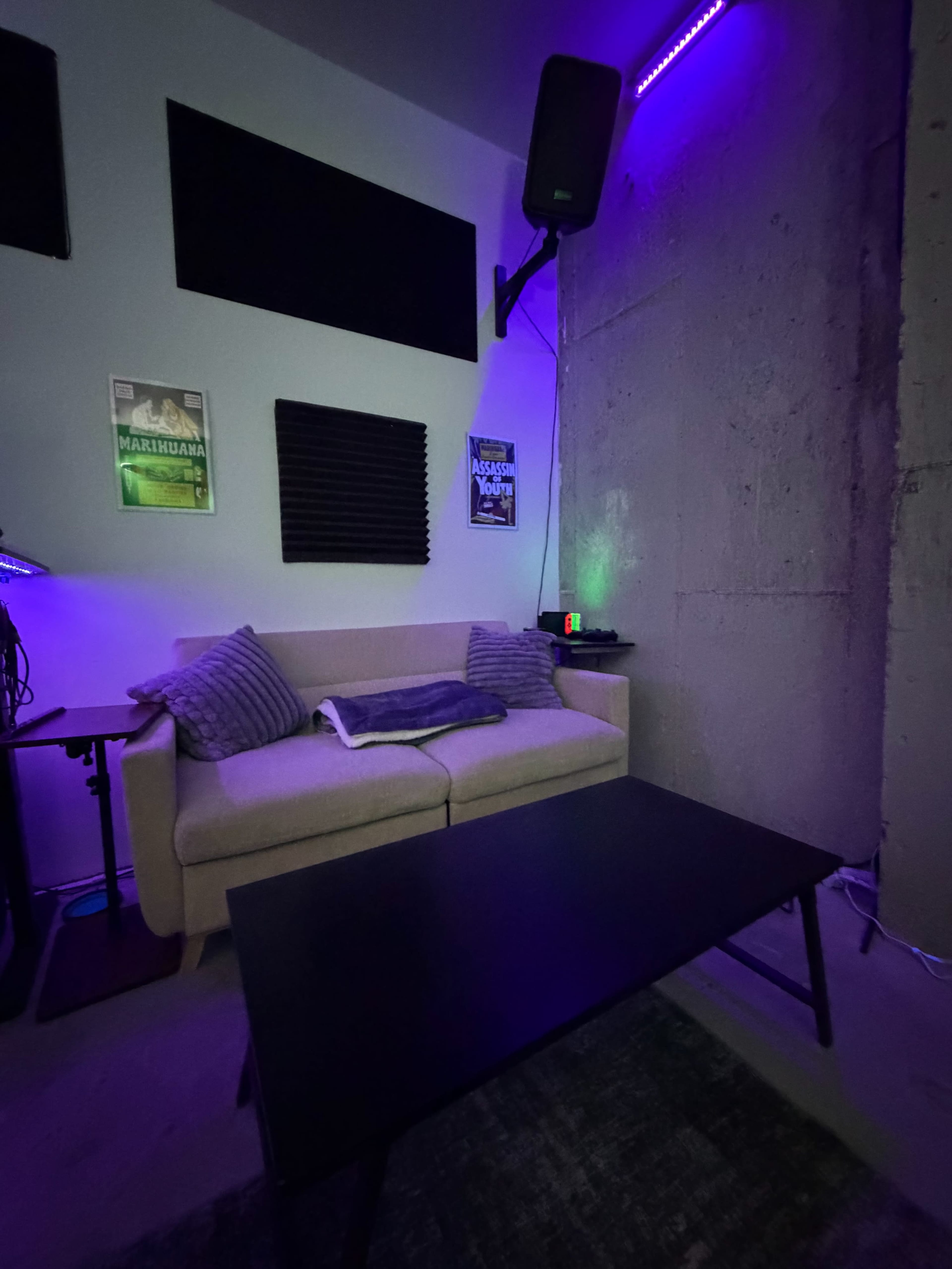 The image shows a room with a couch, a low coffee table, and purple ambient lighting, along with textured walls and various sound equipment.