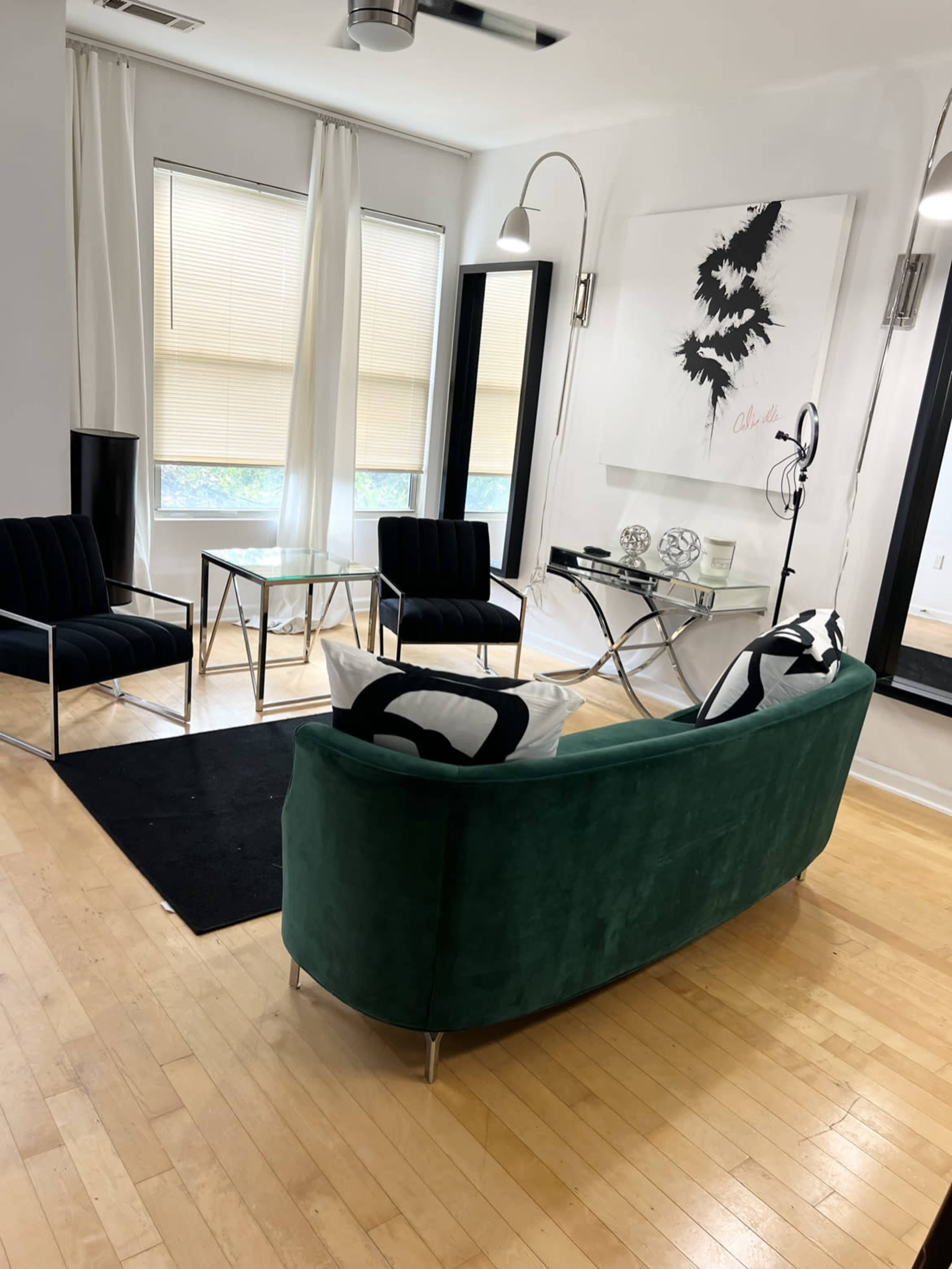 A modern living room with a green curved sofa, two black armchairs, a glass coffee table, and abstract wall art.