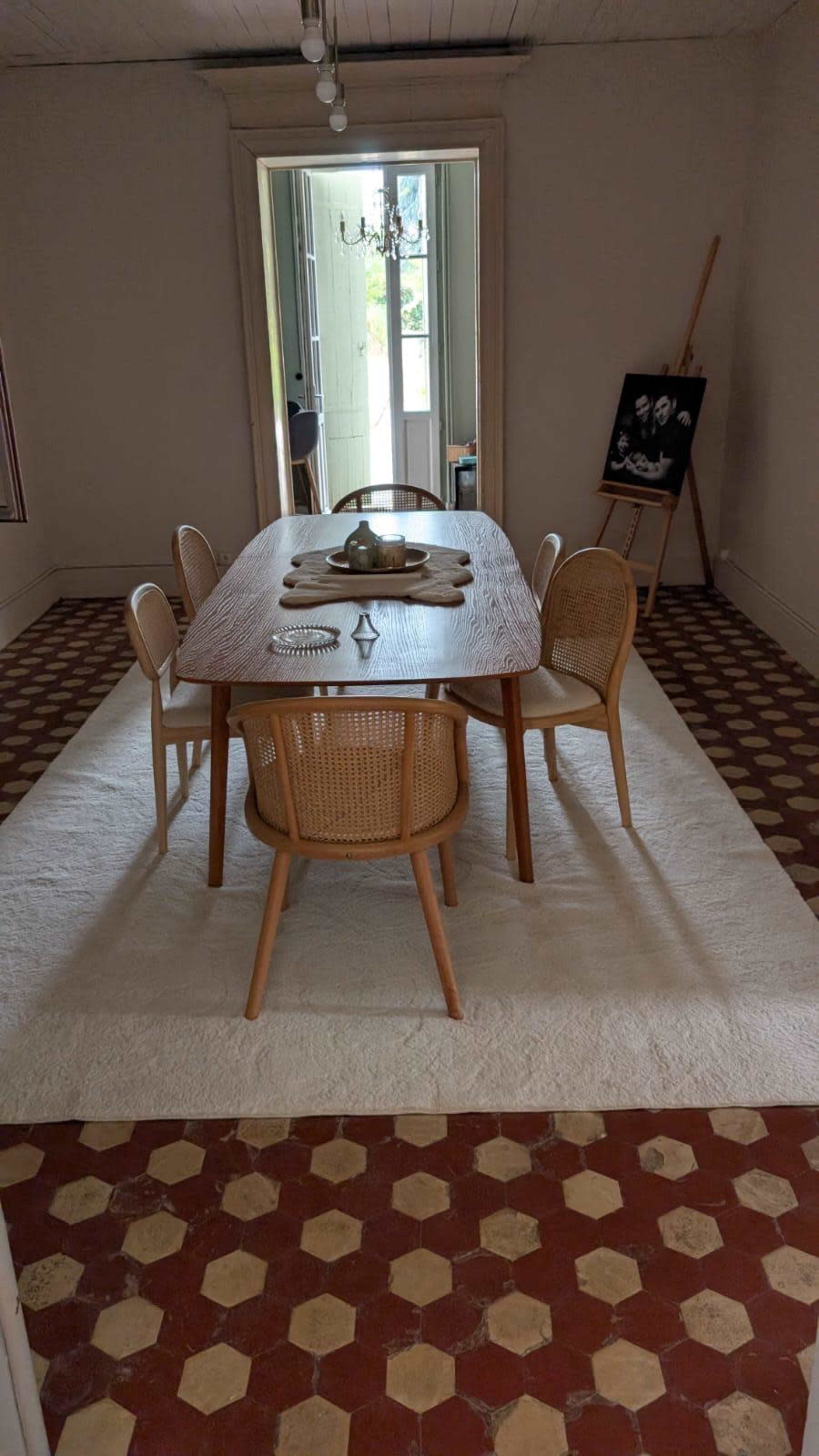 A dining room features a wooden table surrounded by four chairs, with a large mirror and an easel displaying a photo in the background.