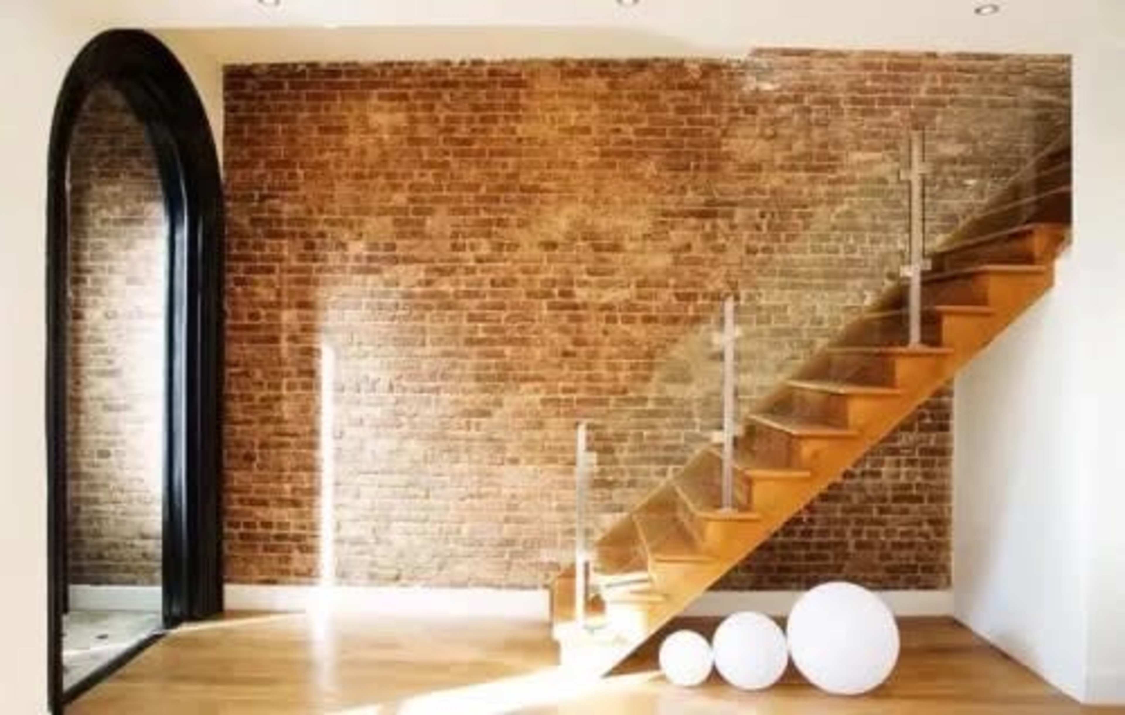 The image features a wooden staircase leading up beside a brick wall and a large black mirror, with three white spherical objects on the floor.