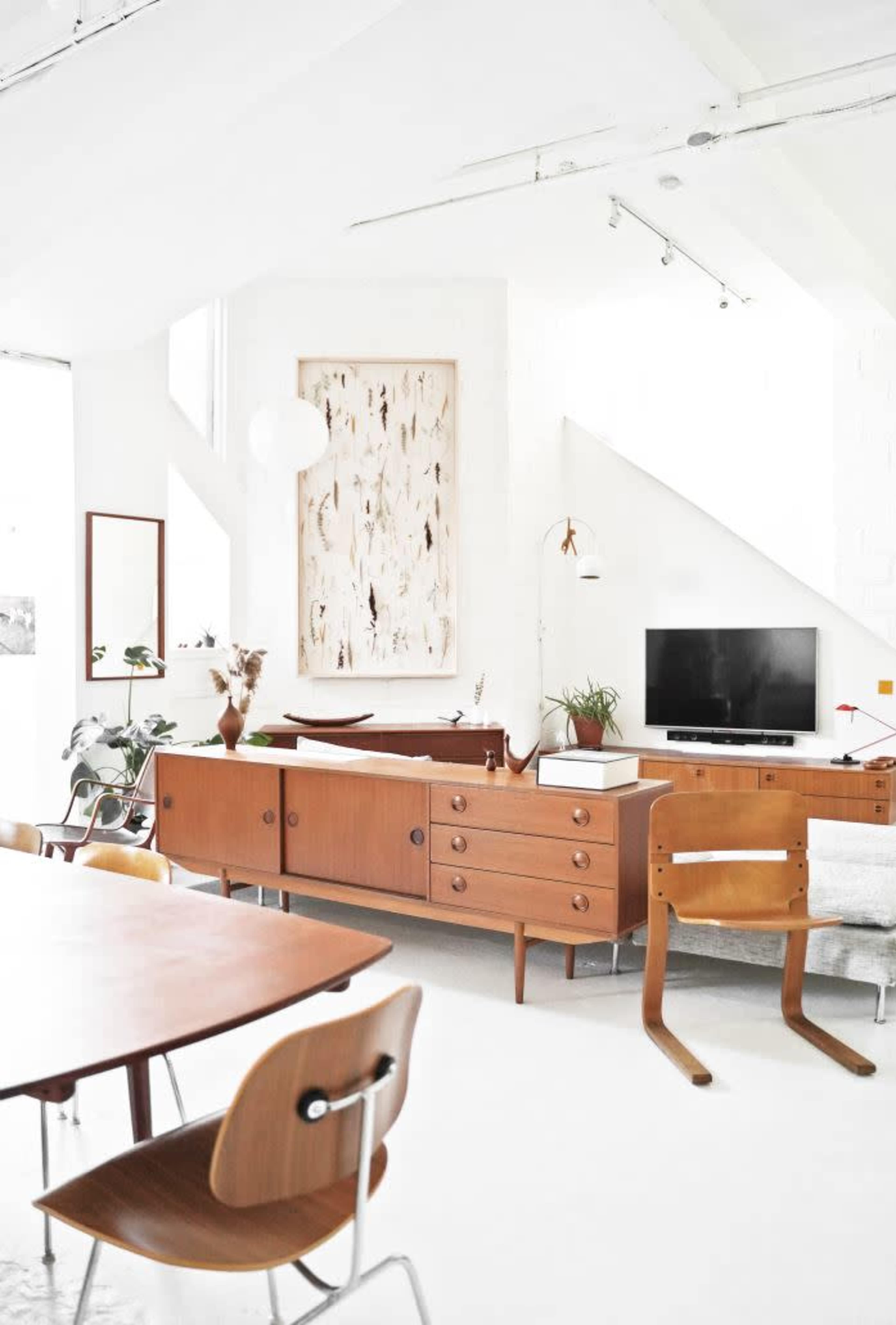 A modern living space with wooden furniture, a TV, and decorative wall art in a light-filled room.