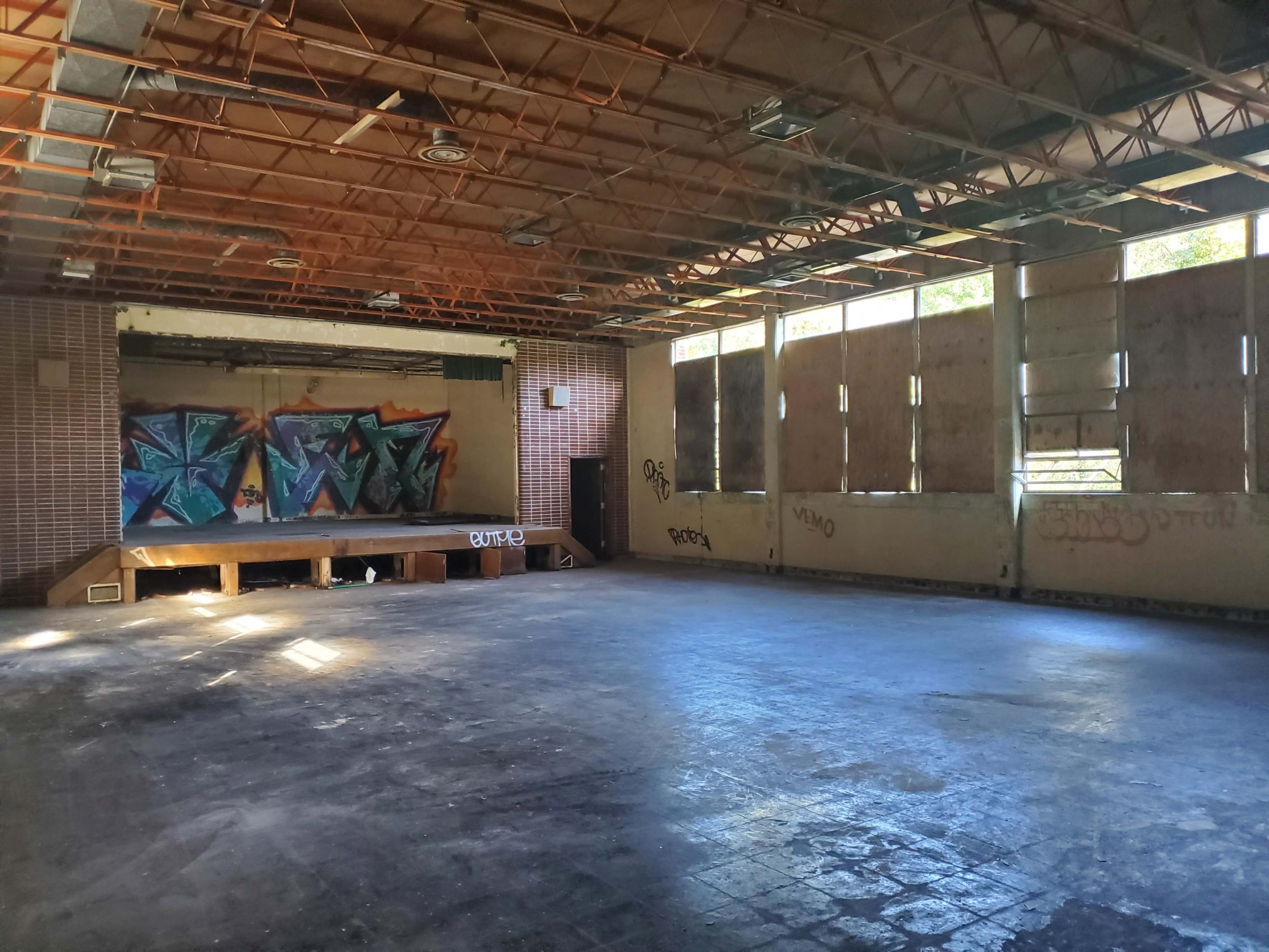 The interior of an abandoned building features dark flooring, empty walls, broken windows, and graffiti art on one side.