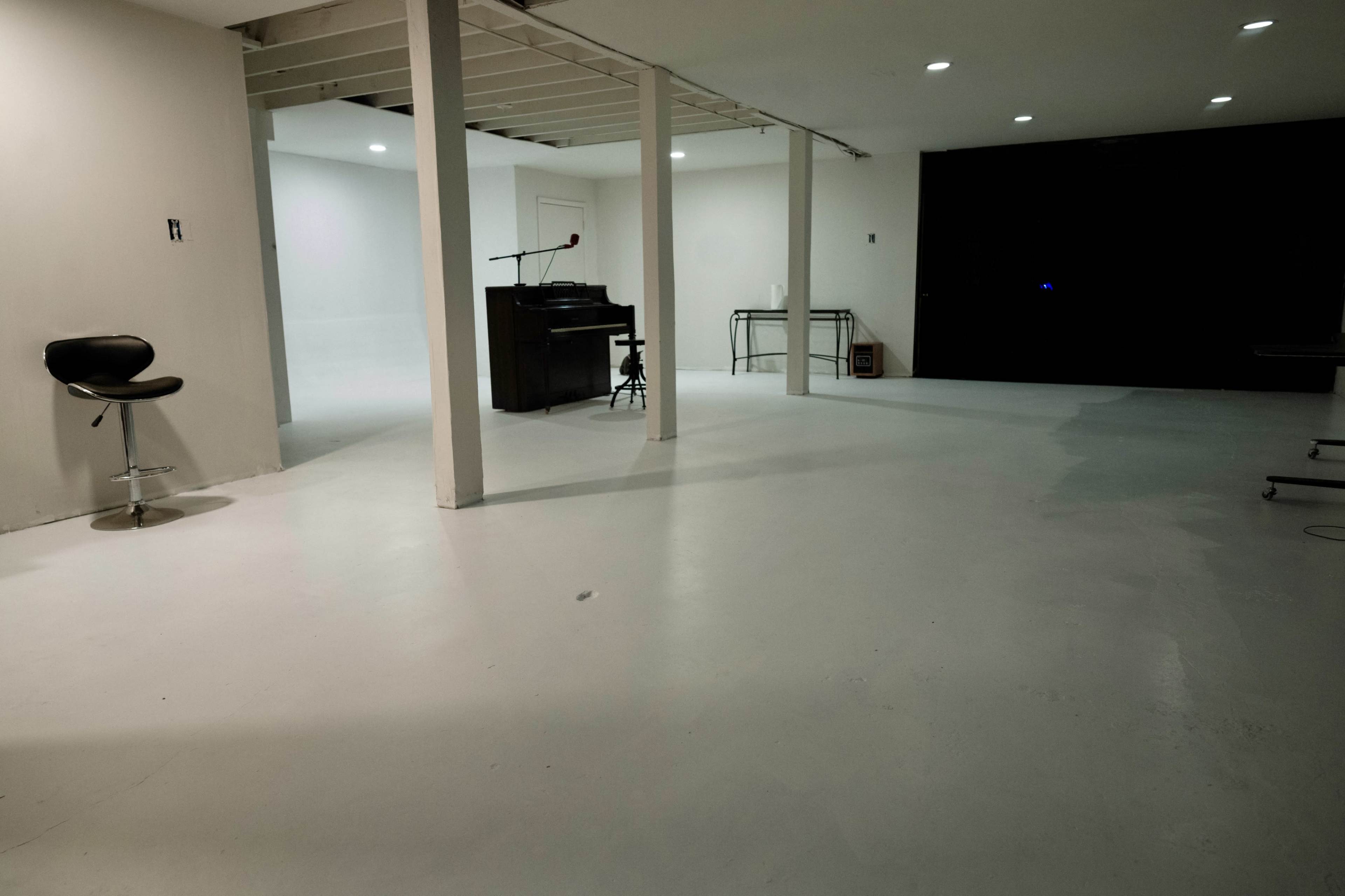 A spacious, minimalist room with white walls, a polished floor, and a piano placed against one wall.
