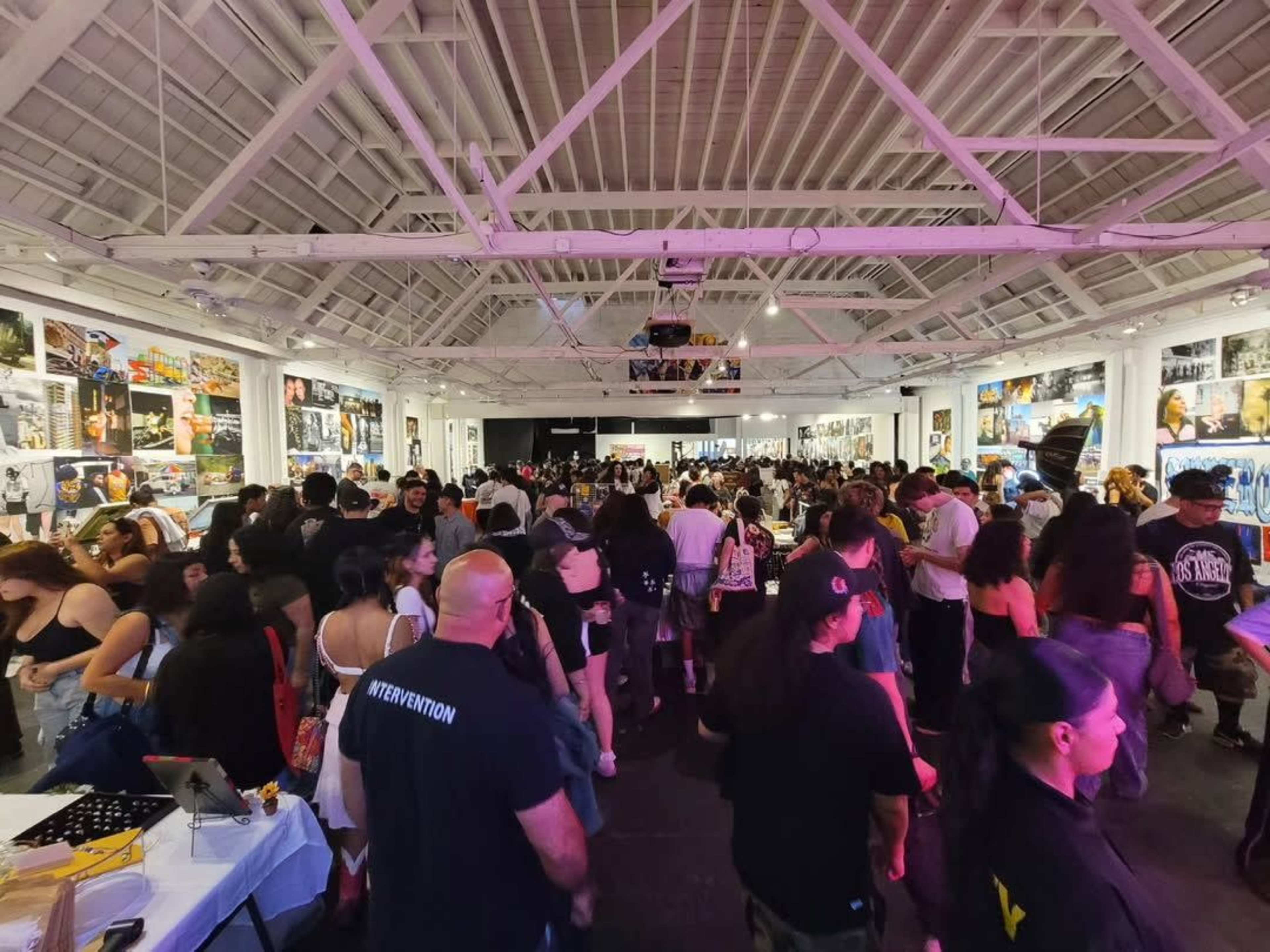 A large crowd of people gathers in a spacious gallery filled with photographs displayed on the walls.