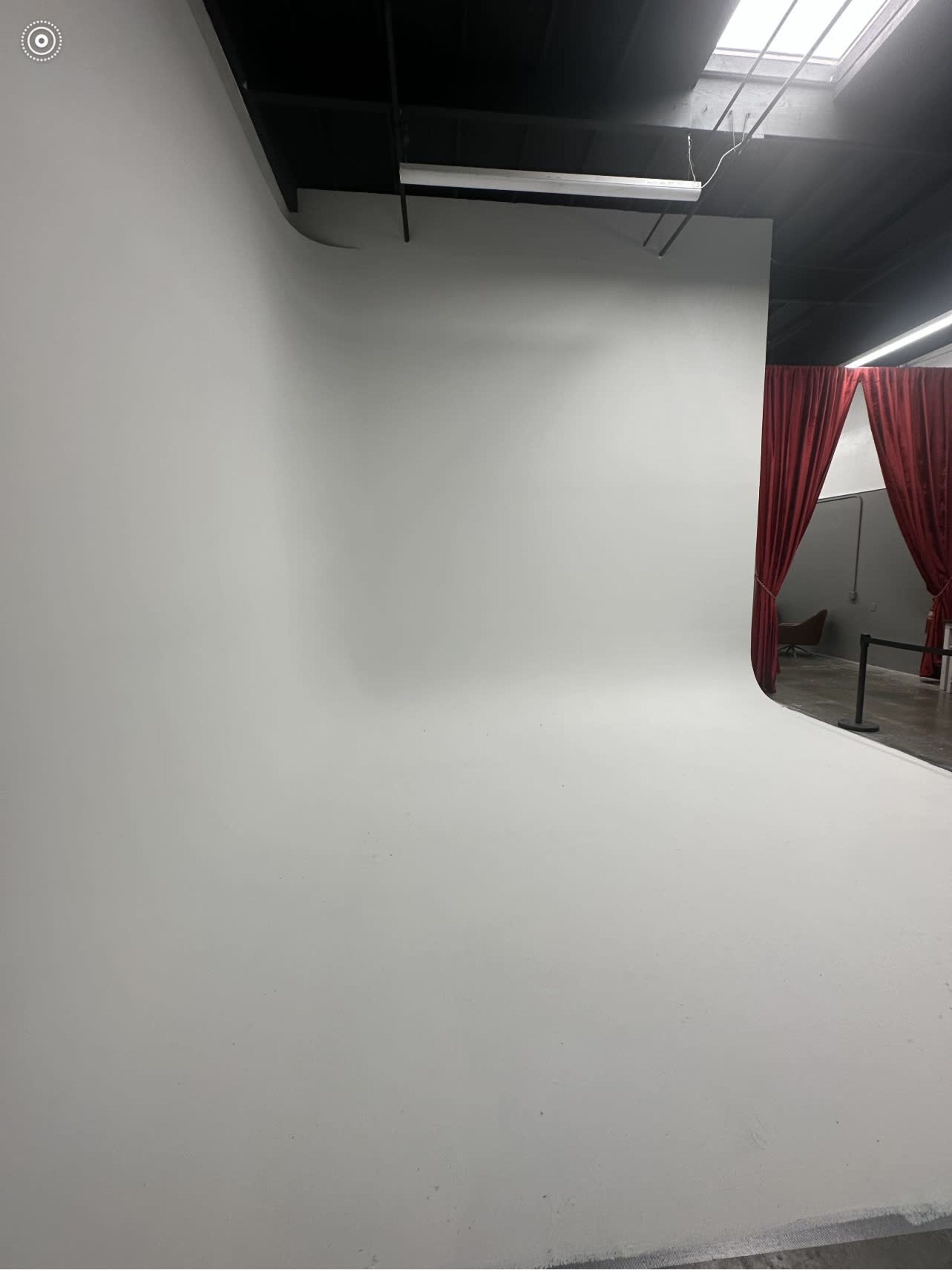 A photography studio featuring a seamless white backdrop and red curtains in the background.