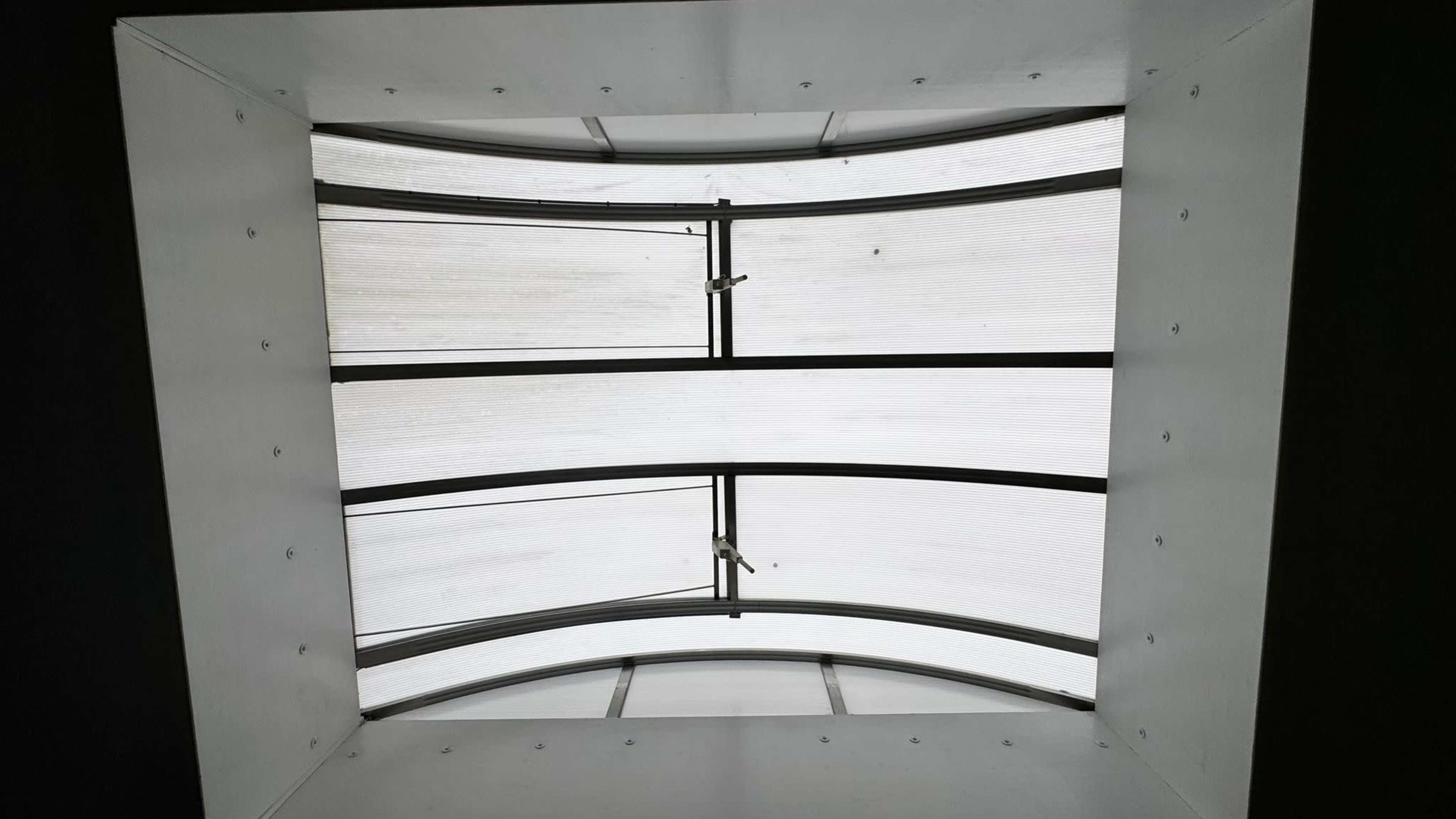 The image shows a rectangular skylight with a curved design, featuring metal frames and a translucent covering.