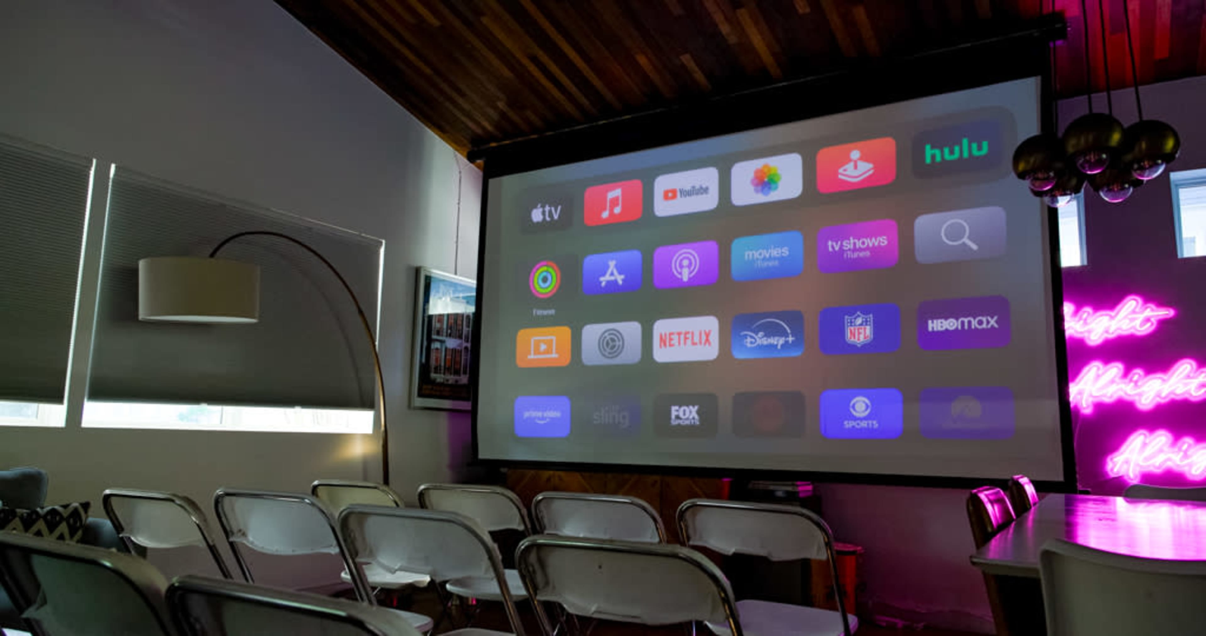 A large projection screen displaying various streaming service icons is set up in a room with rows of empty chairs.